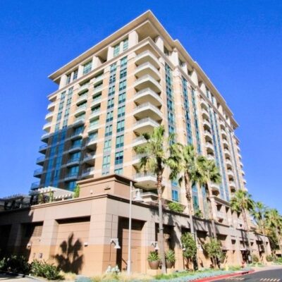 Exterior daytime view of one of The Plaza condominium towers, featuring glass balconies and palm-lined streets.