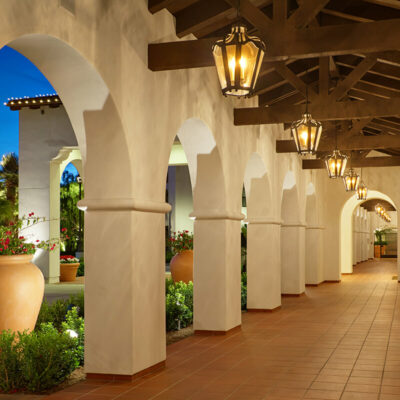 Covered walkway with white arches, terracotta flooring, hanging lanterns, and lush landscaping.