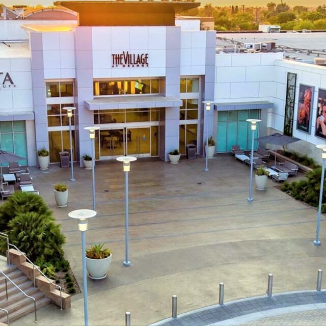 Aerial perspective of the mall entrance plaza with potted plants, patio umbrellas, and The Village at Orange signage.