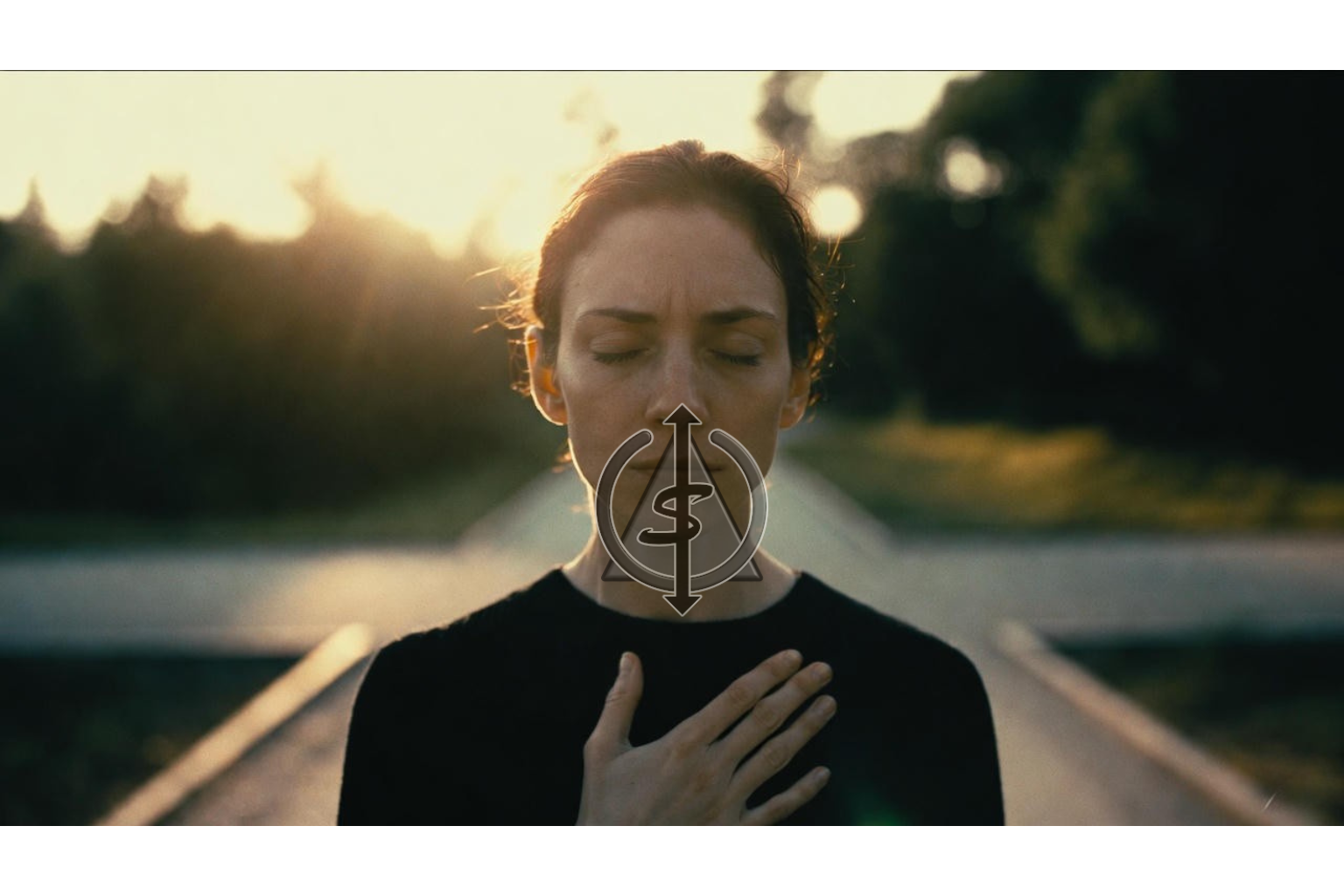 Person standing at a crossroads at sunrise with hand over their heart, pausing to trust their inner knowing before choosing a direction.