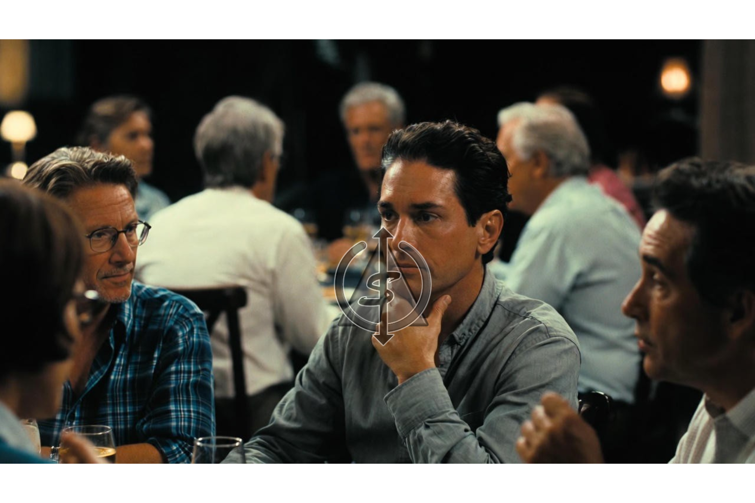 Person sitting at a busy dinner table quietly looking down with a hand near their throat, symbolizing staying silent to keep others comfortable.