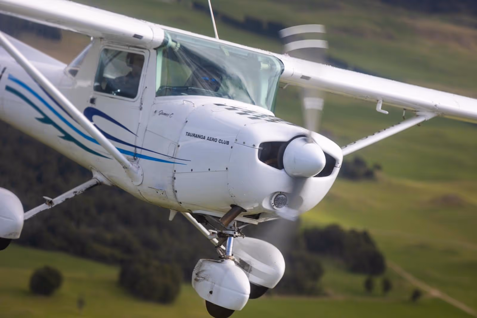 White single-engine propeller airplane flying low over a green landscape.