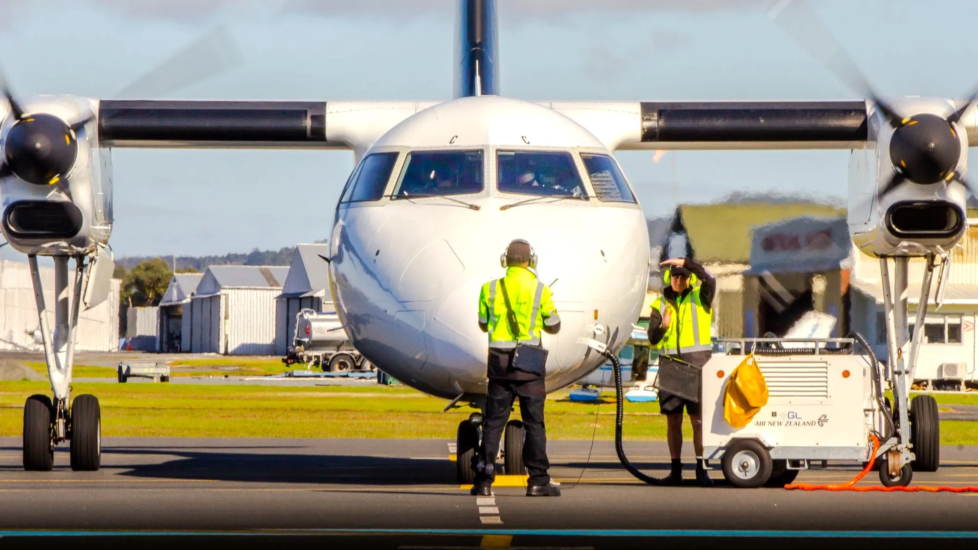 Ground crew in yellow safety vests preparing a twin-engine propeller airplane on the runway at an airport.