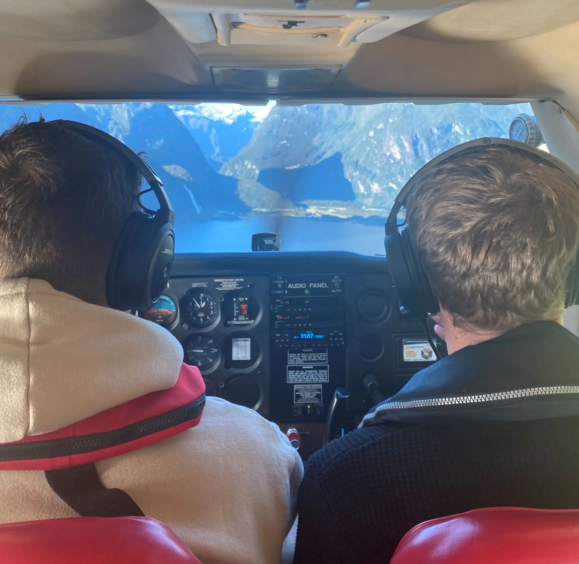 Two people wearing headsets flying a small plane over a mountain lake.