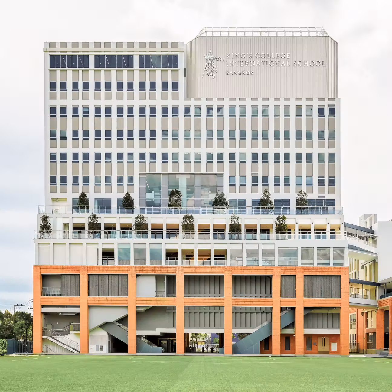 Modern multi-story building of King's College International School Bangkok with a green sports field in front.