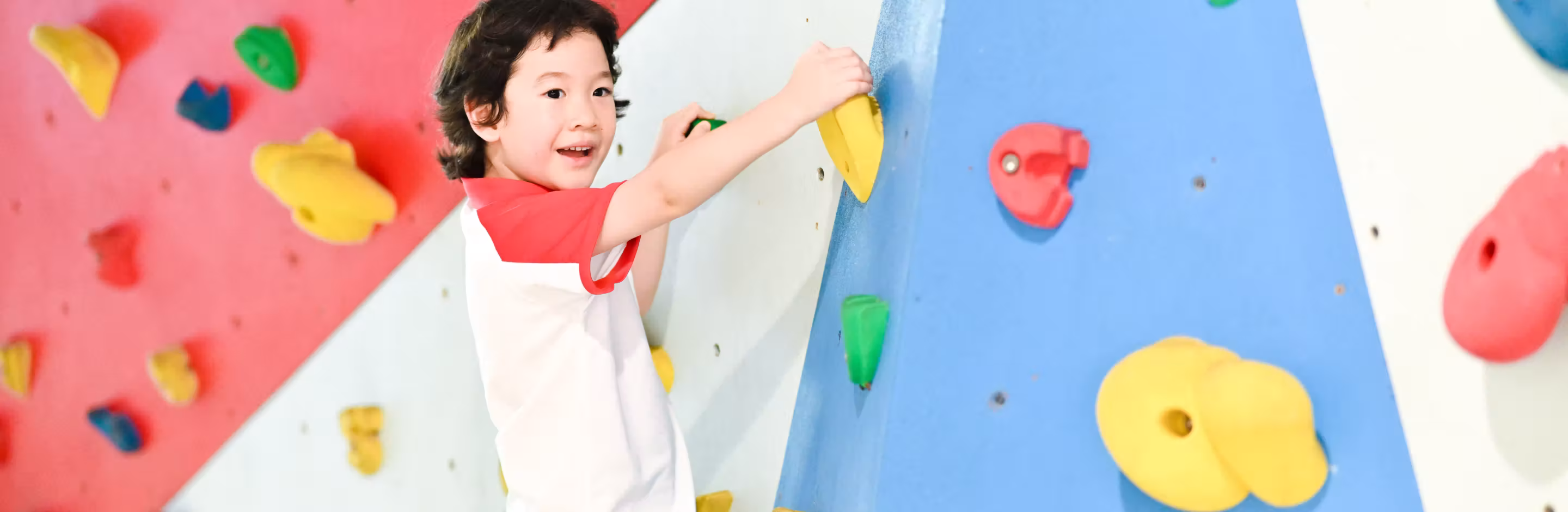 Young child climbing a colorful indoor rock climbing wall with red, blue, yellow, and green holds.