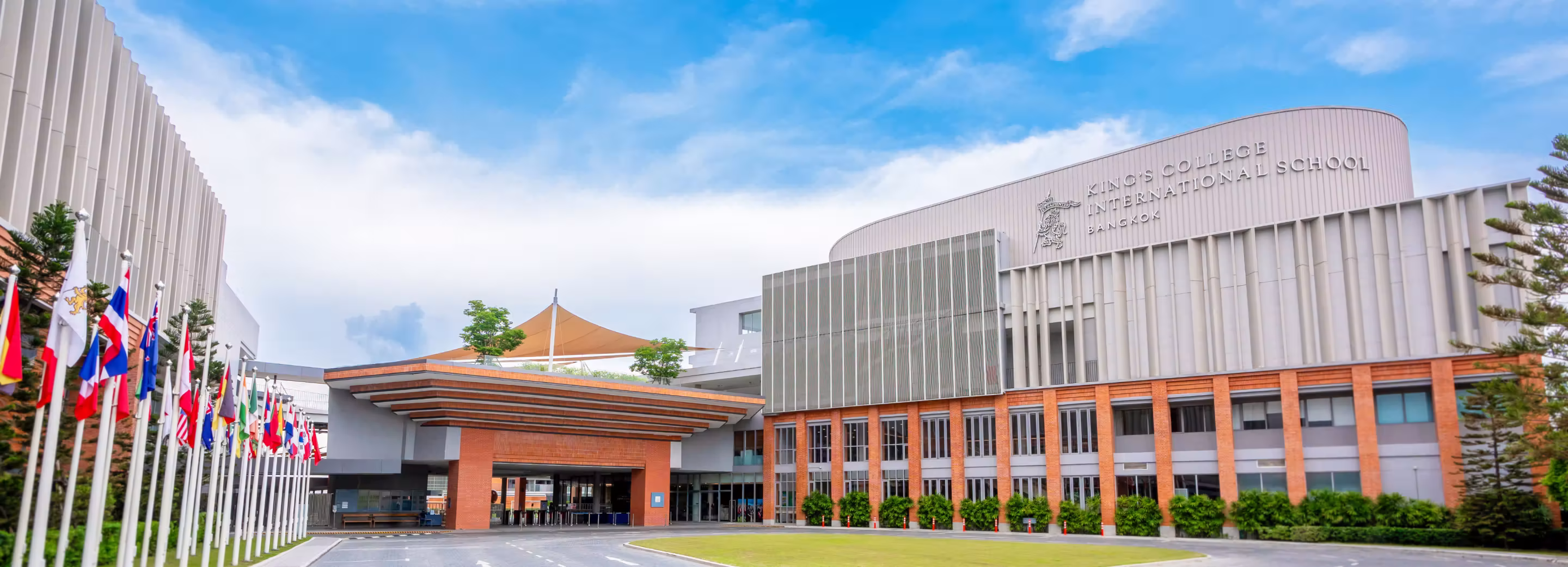 Modern building of King's College International School Bangkok with several international flags lined up on poles to the left.