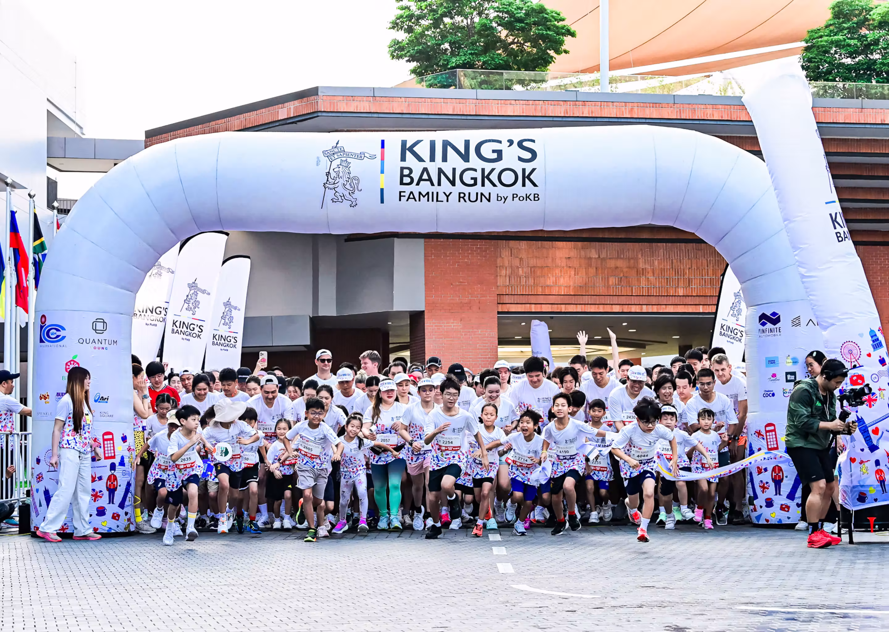 Crowd of children and adults running a family race under an inflatable King's Bangkok start arch.