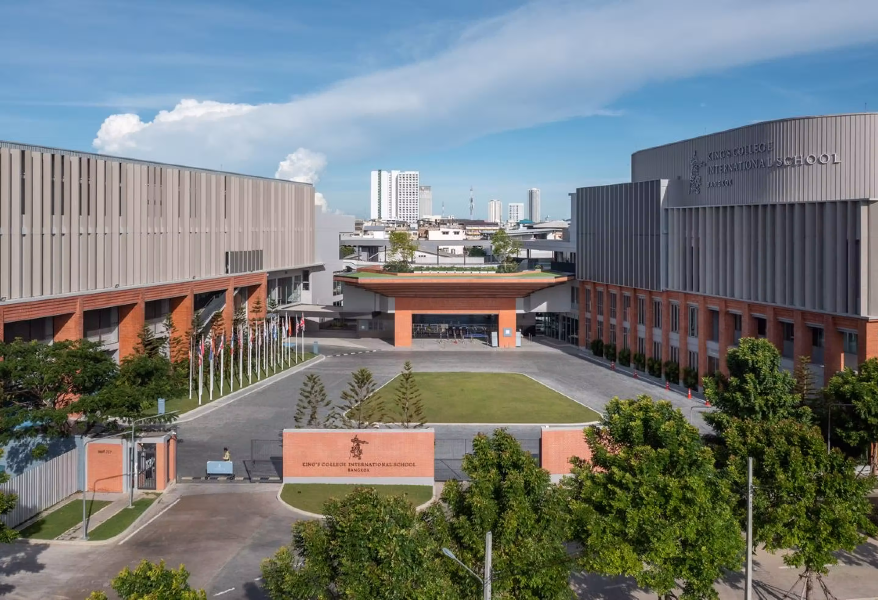 Entrance of King’s College International School Bangkok with modern buildings and flagpoles under a clear sky.