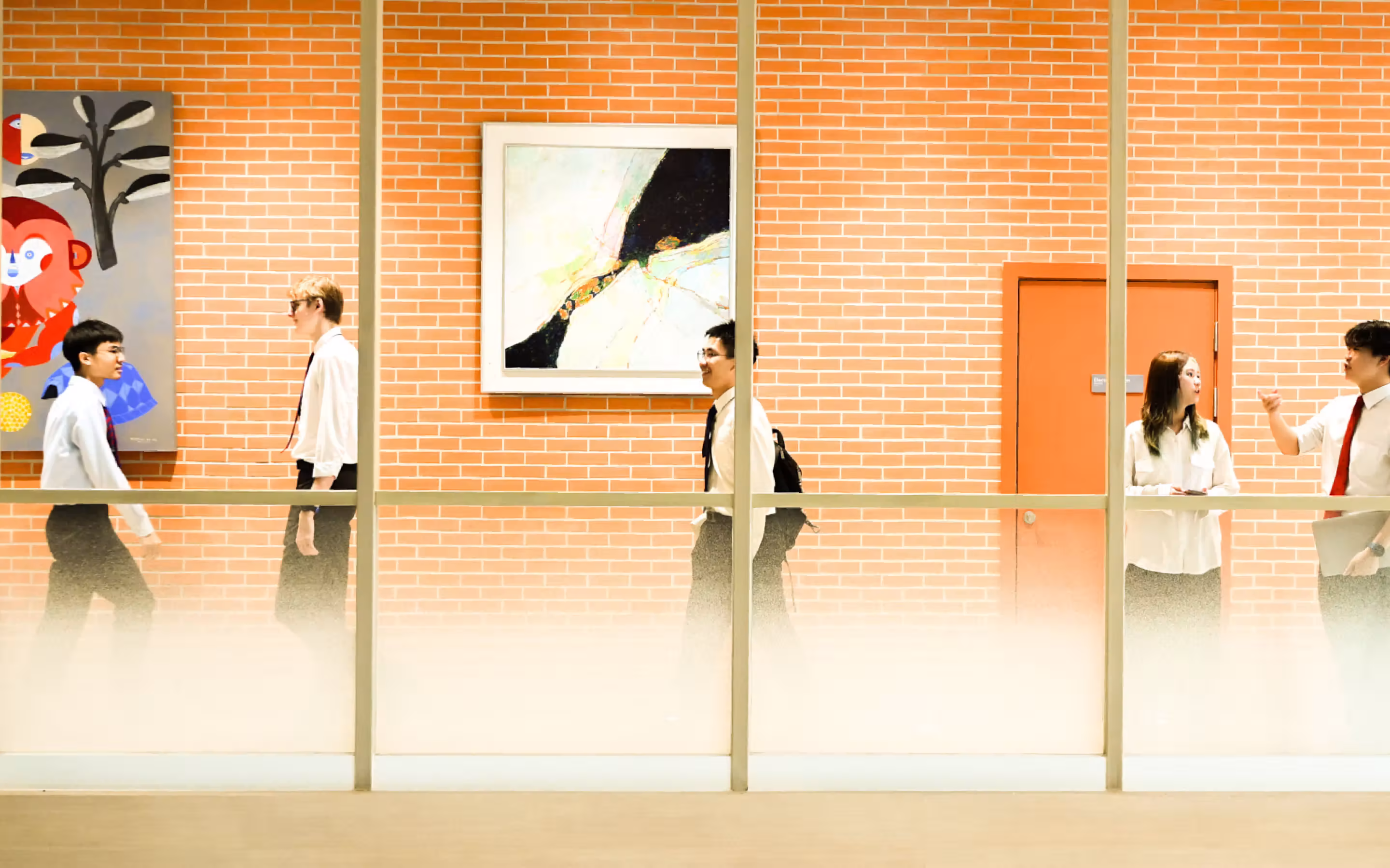 Five people in business attire walking and talking inside a building with brick walls and framed art.