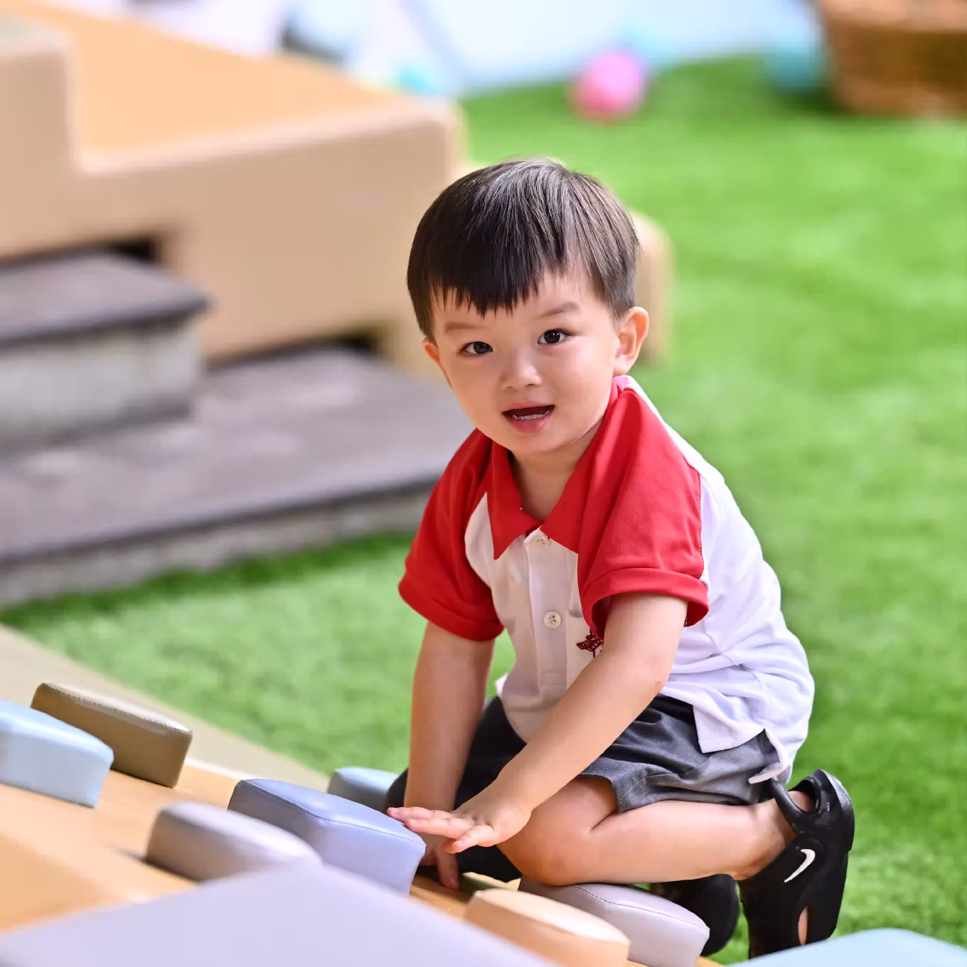 Young boy in red and white shirt playing on colourful stepping stones outdoors on green grass.