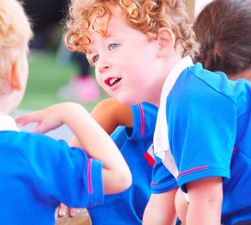 Young children in blue school uniforms engaging in conversation outdoors.
