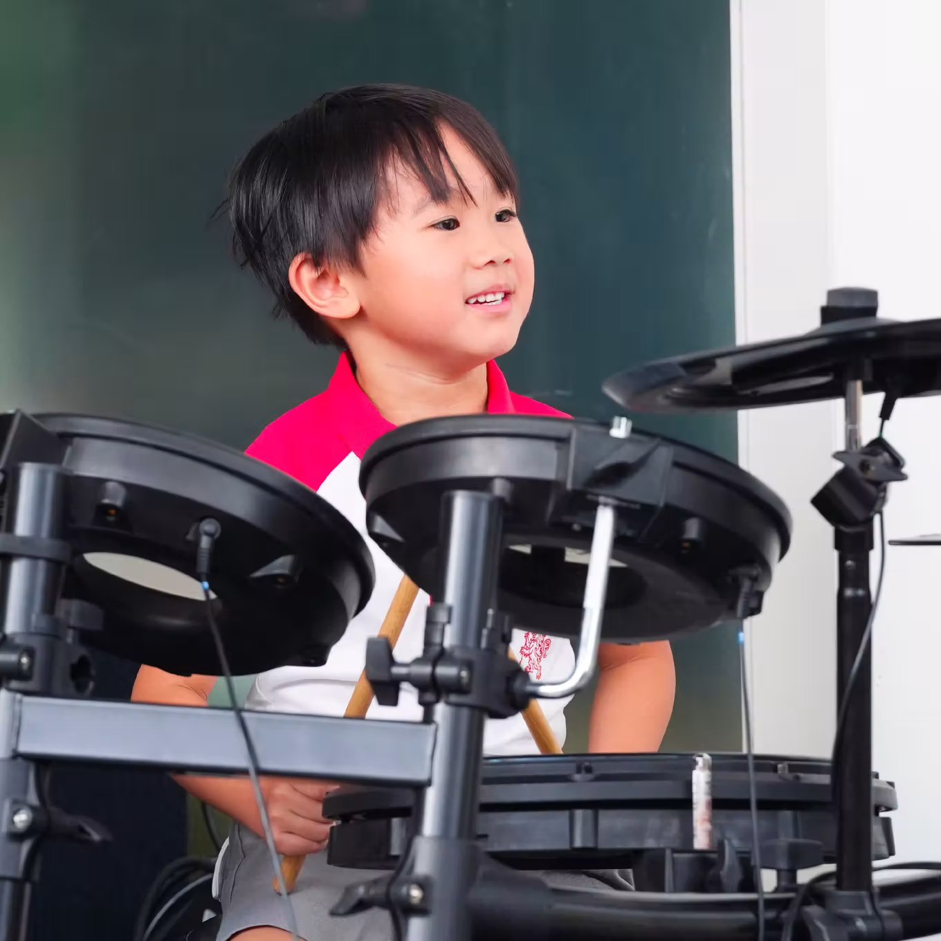 Young boy smiling and playing an electronic drum set indoors.