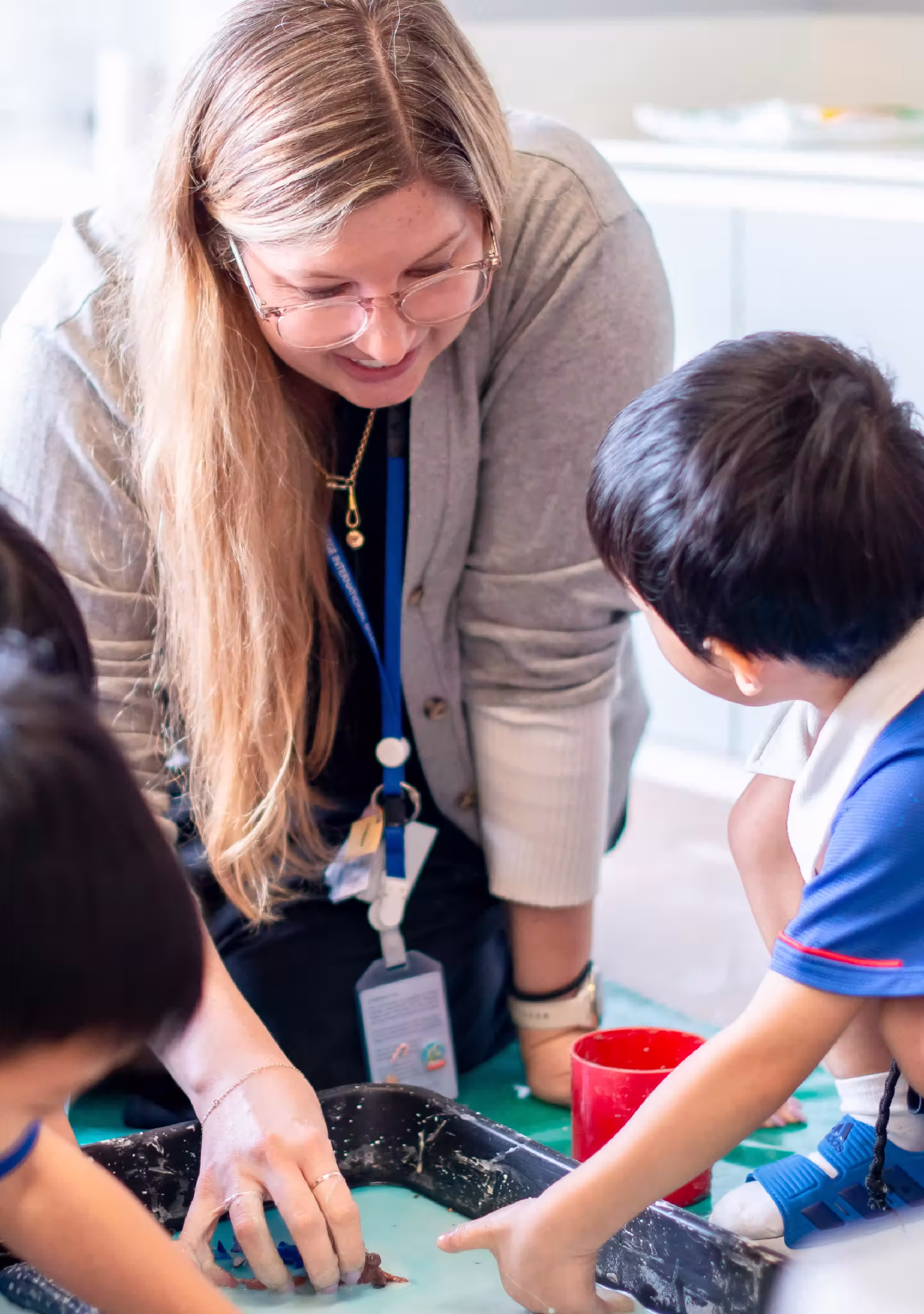 Teacher and children engaged in a hands-on activity with a tray of blue liquid and objects.