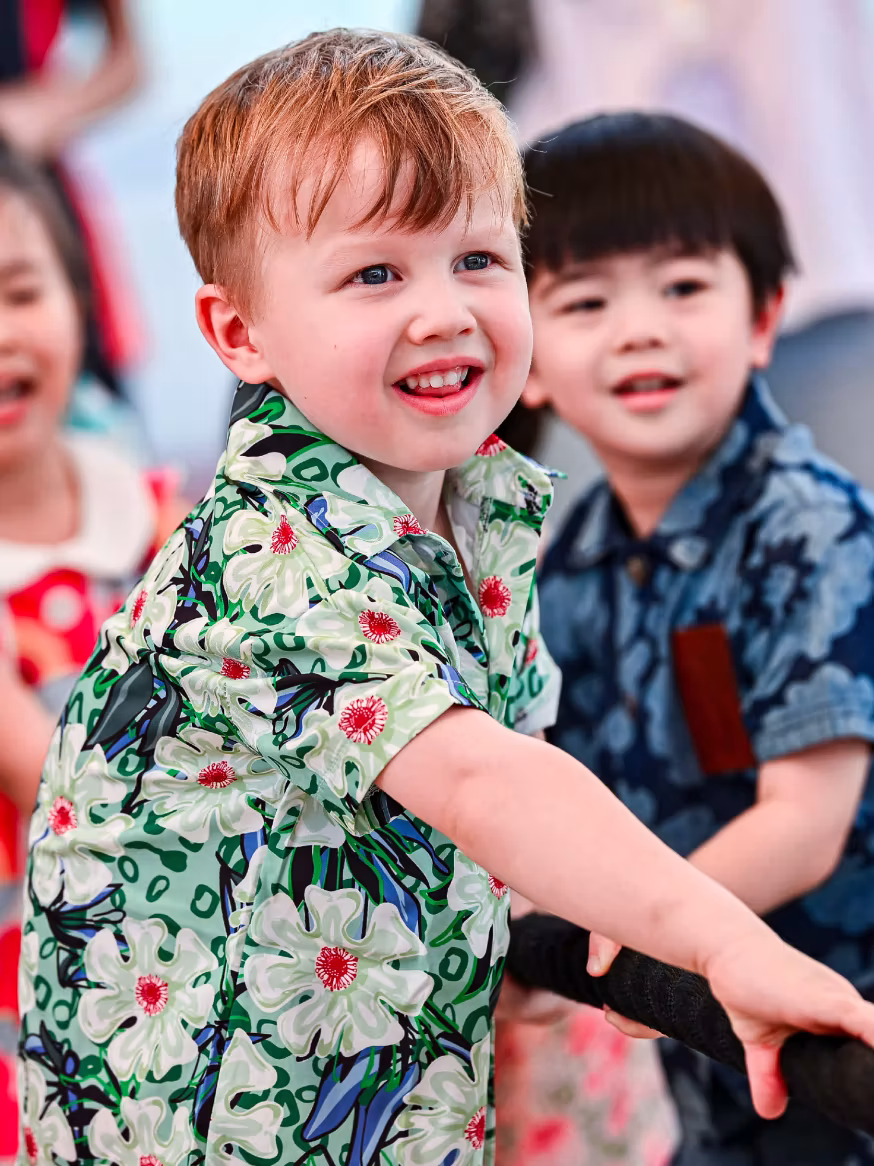 Smiling children playing tug-of-war, boy in floral green shirt is pulling the rope.