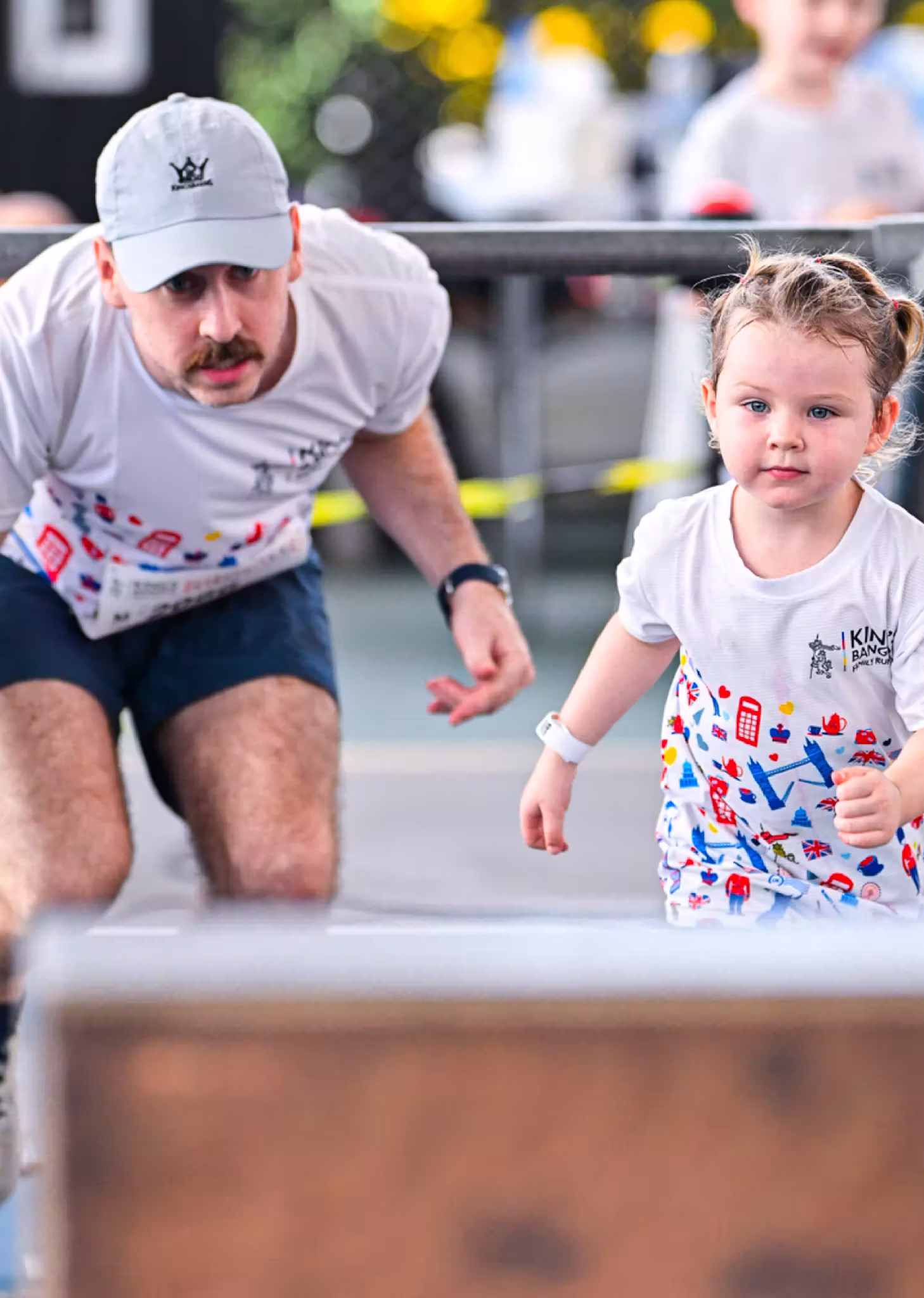 Young girl and man running together in a race, both wearing matching printed white shirts.