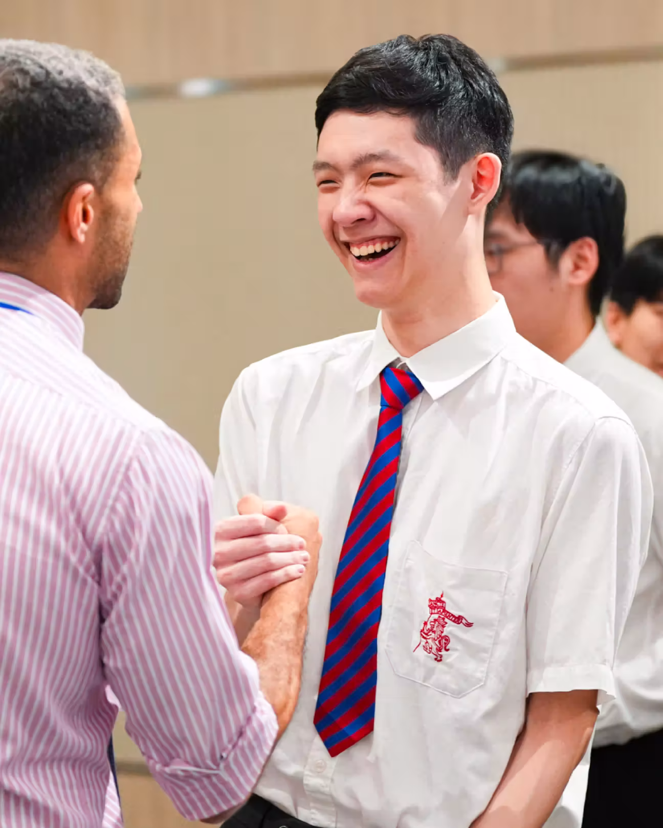 Two men shaking hands, one smiling broadly in a white shirt and striped red-blue tie.