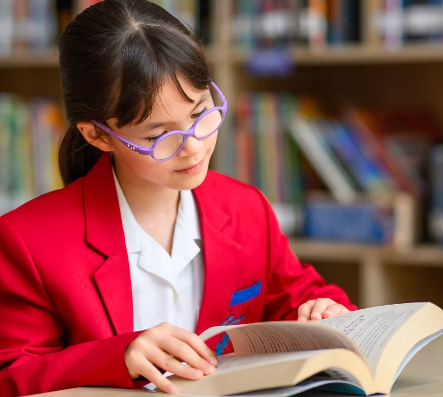 Young girl with purple glasses reading a book in a library.