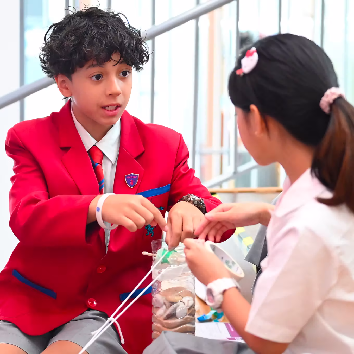 Two school children working together on a science experiment with a plastic bottle and tubes.