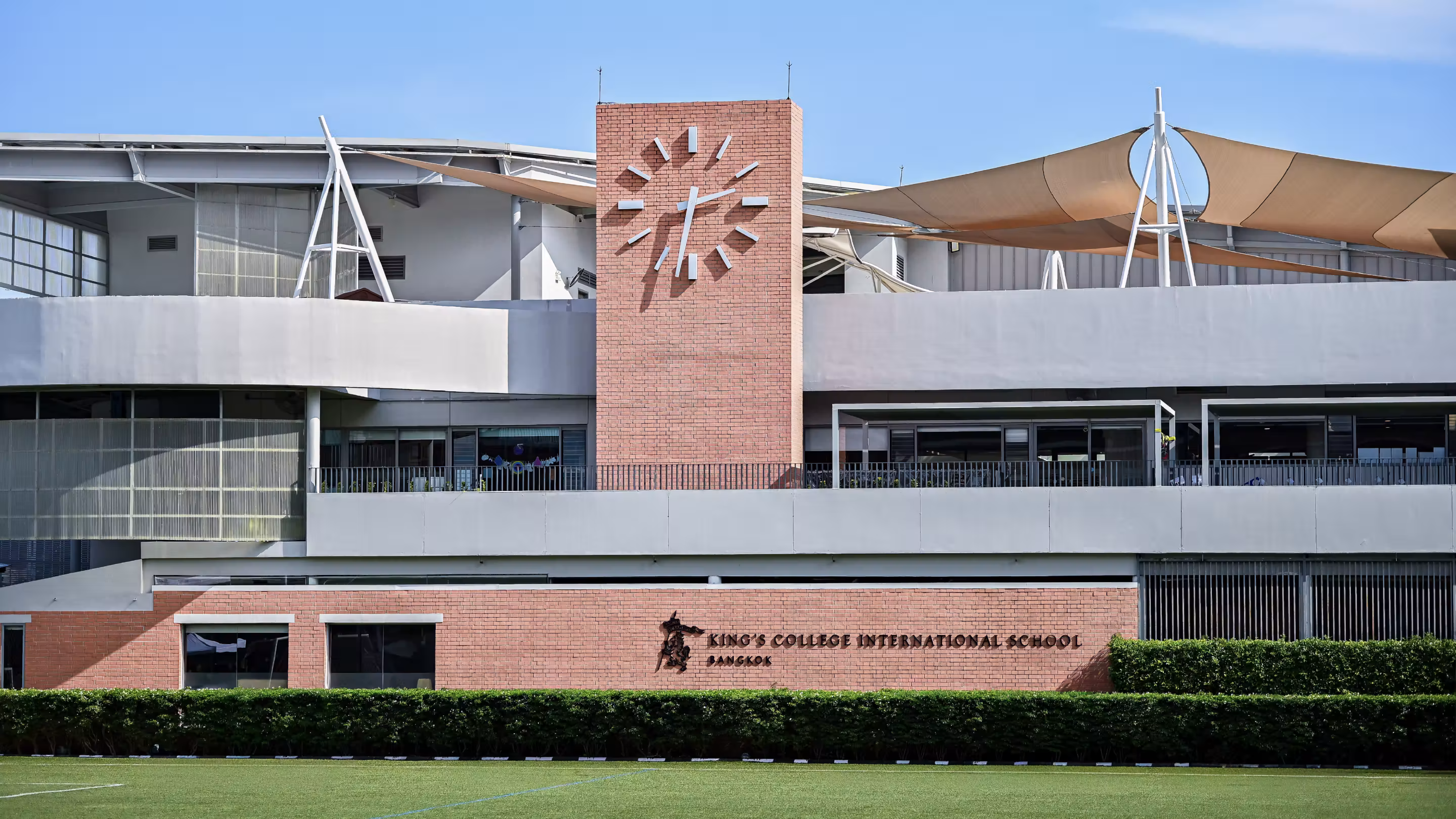 King's College International School Bangkok building with a clock tower and green lawn in front.