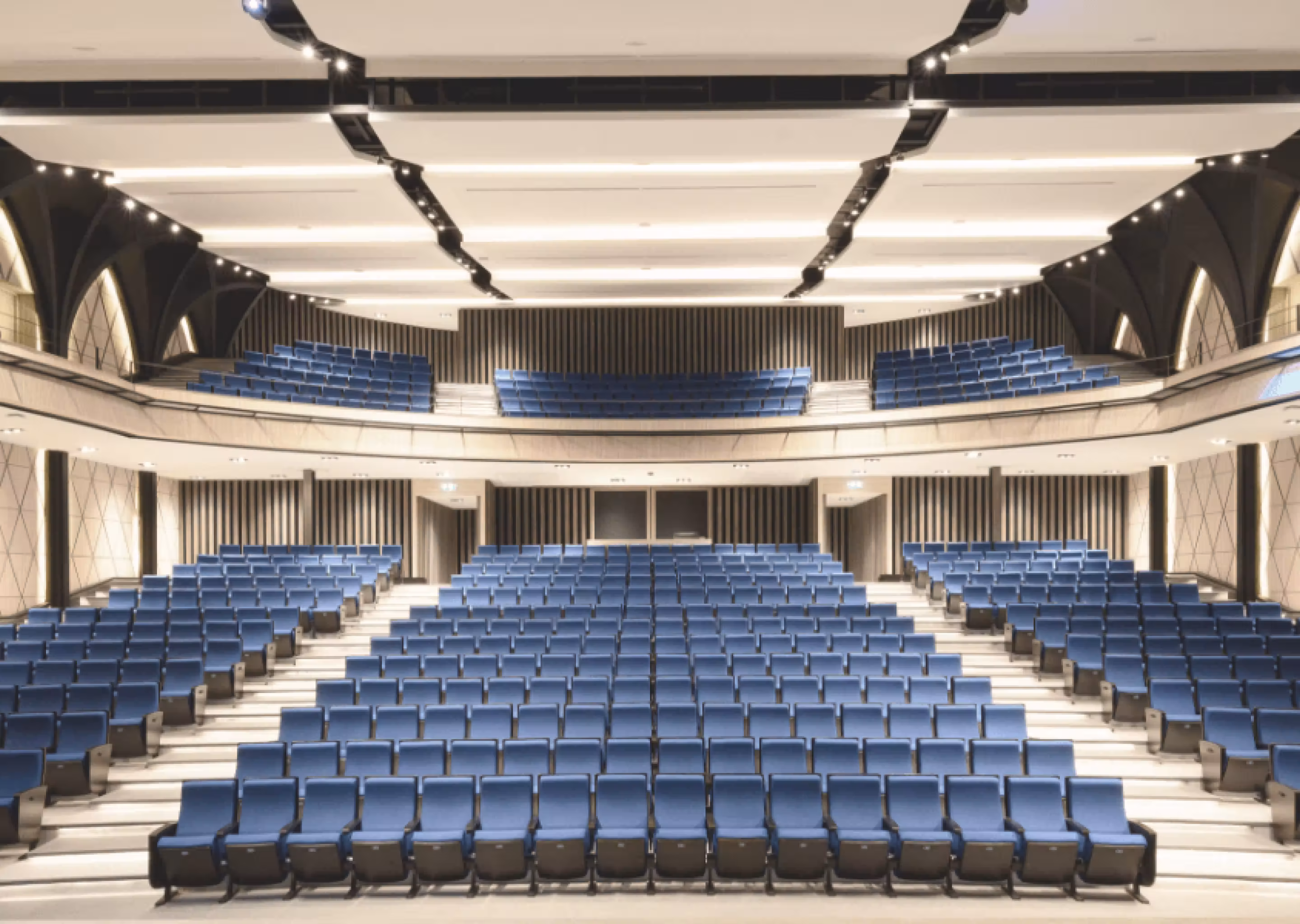 Empty modern auditorium with blue seats arranged on two levels facing front stage area.
