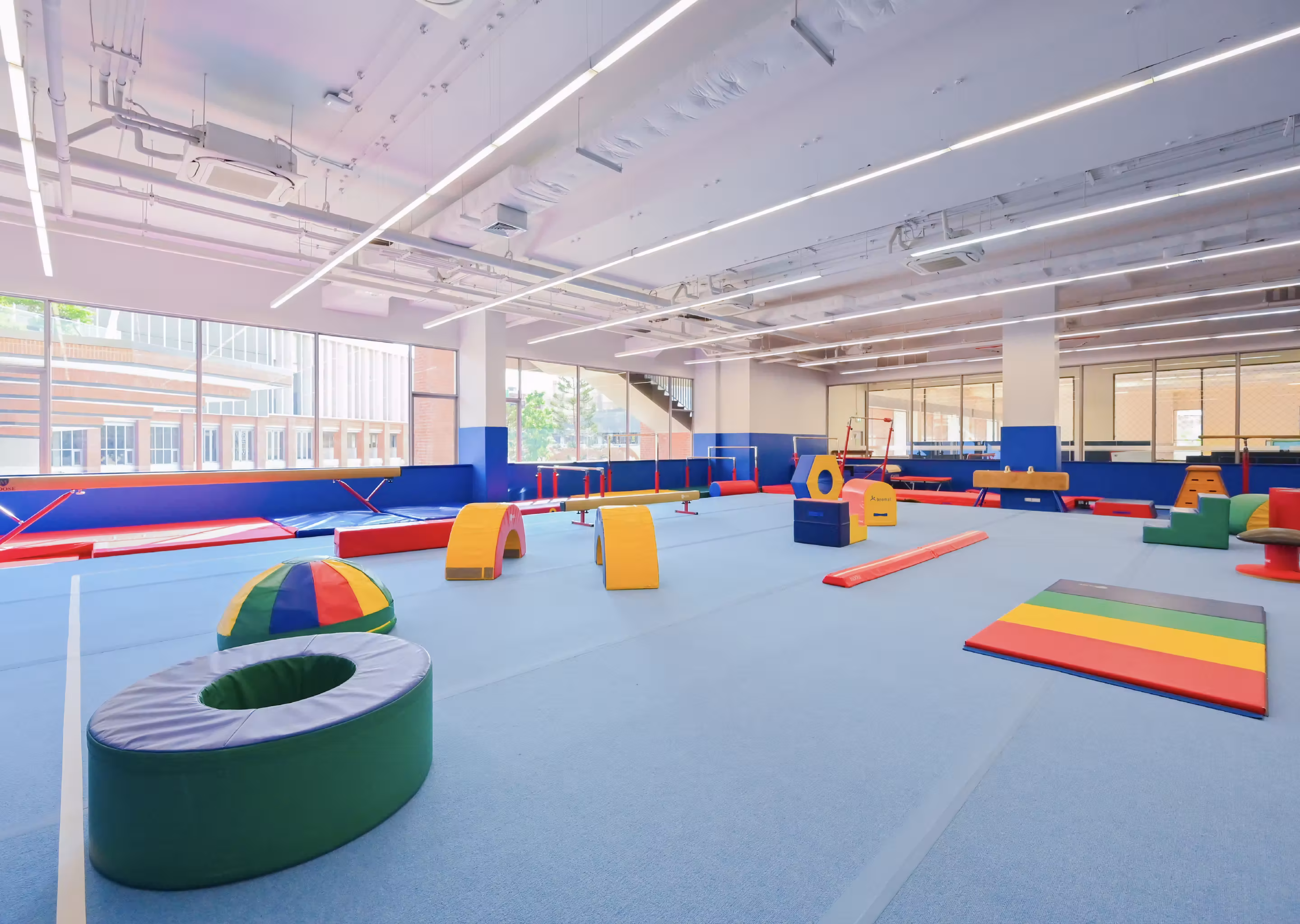 Bright indoor gym with blue floor and colorful soft play equipment for children.