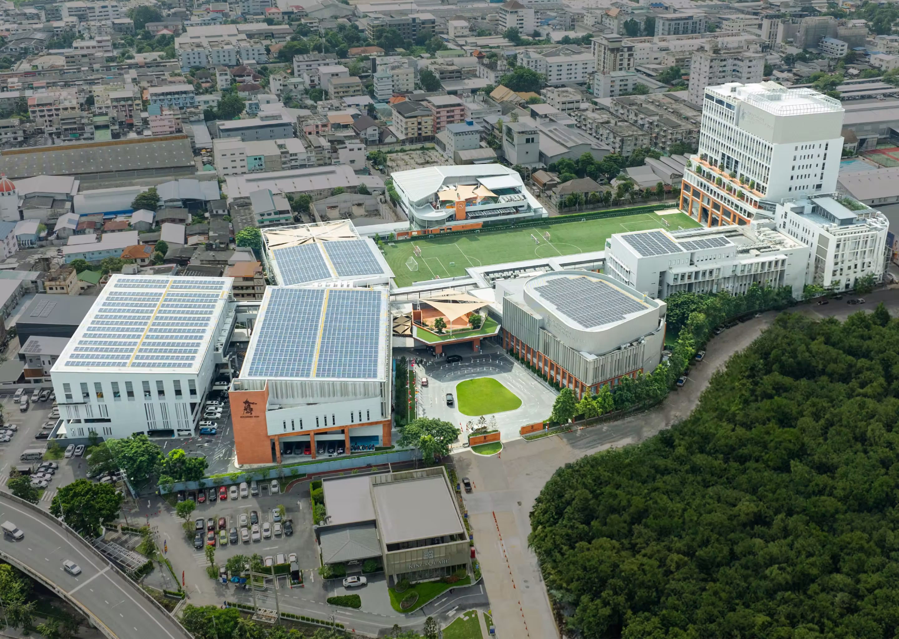 Aerial view of a large school complex with solar panels, sports field, and surrounding buildings.