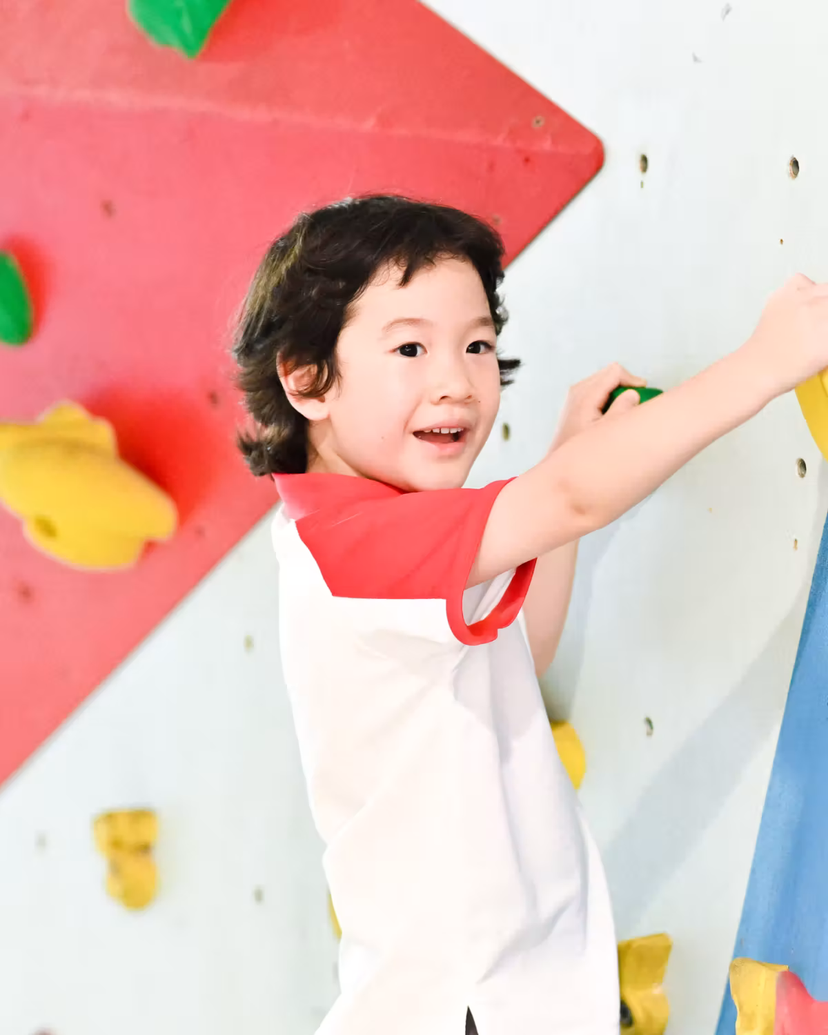 Child climbing an indoor rock climbing wall with colorful handholds, looking happy and focused.