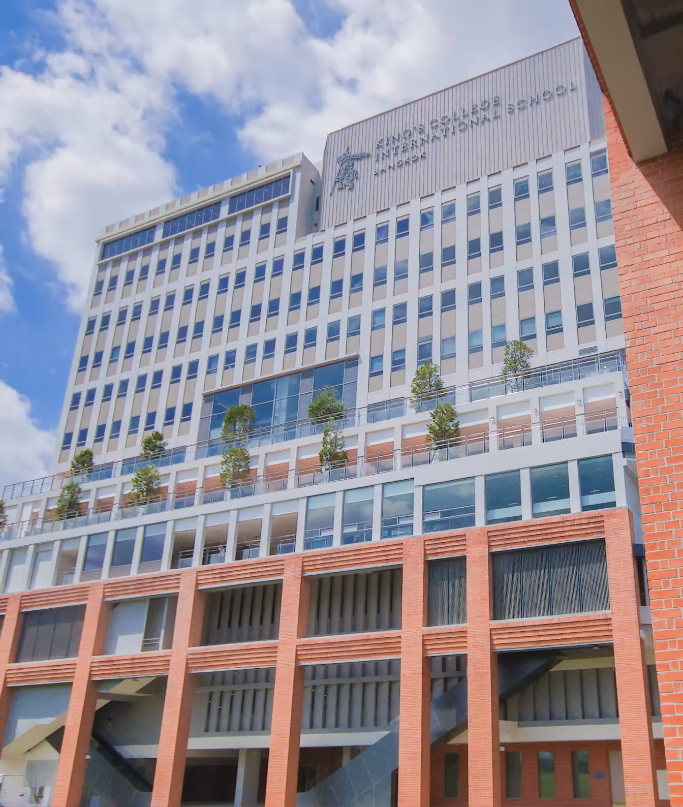 Tall modern building with terraces and trees under a partly cloudy blue sky.