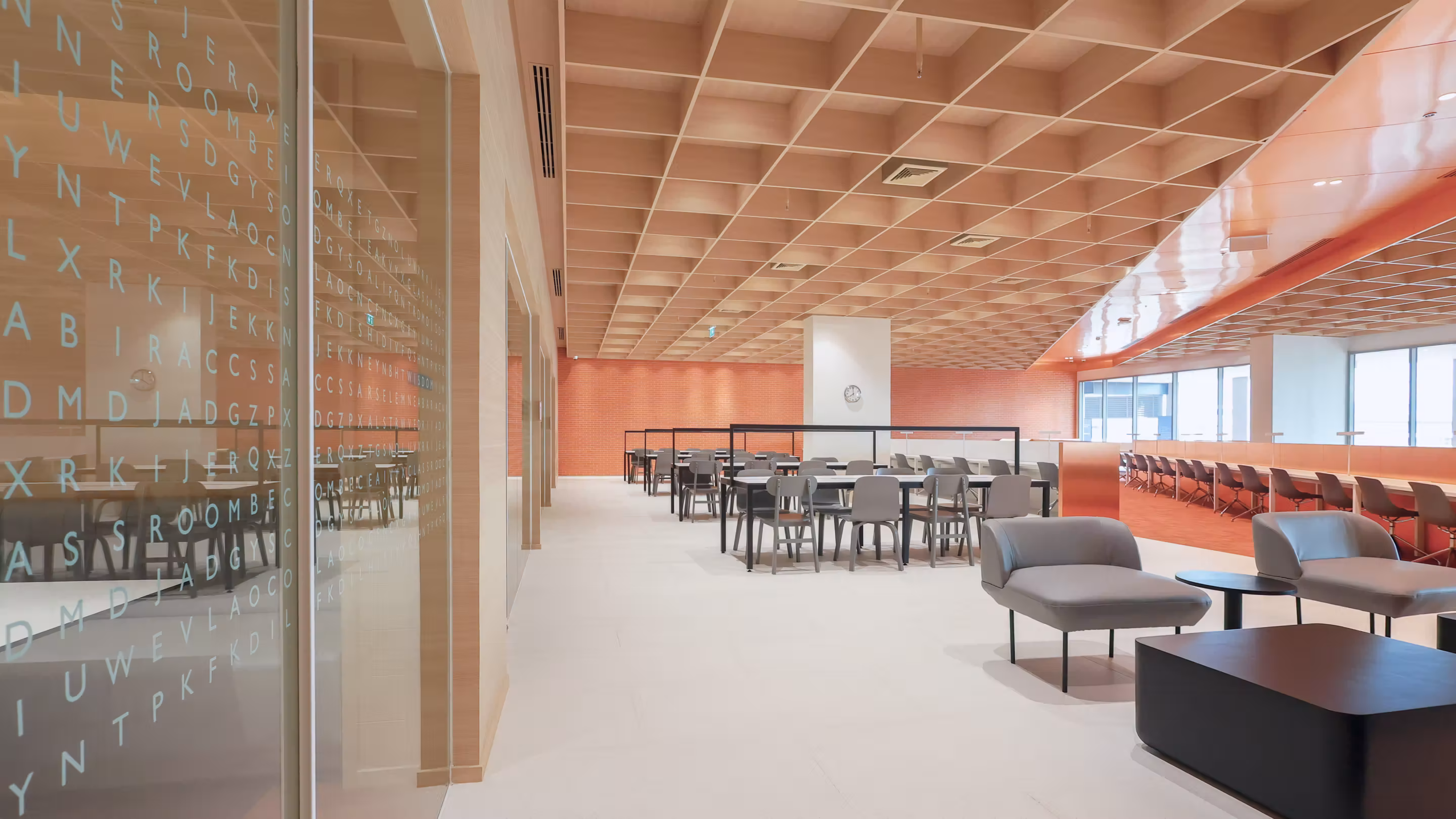 Modern study area with grey chairs, tables, lounge seats, and large windows under a wooden ceiling.