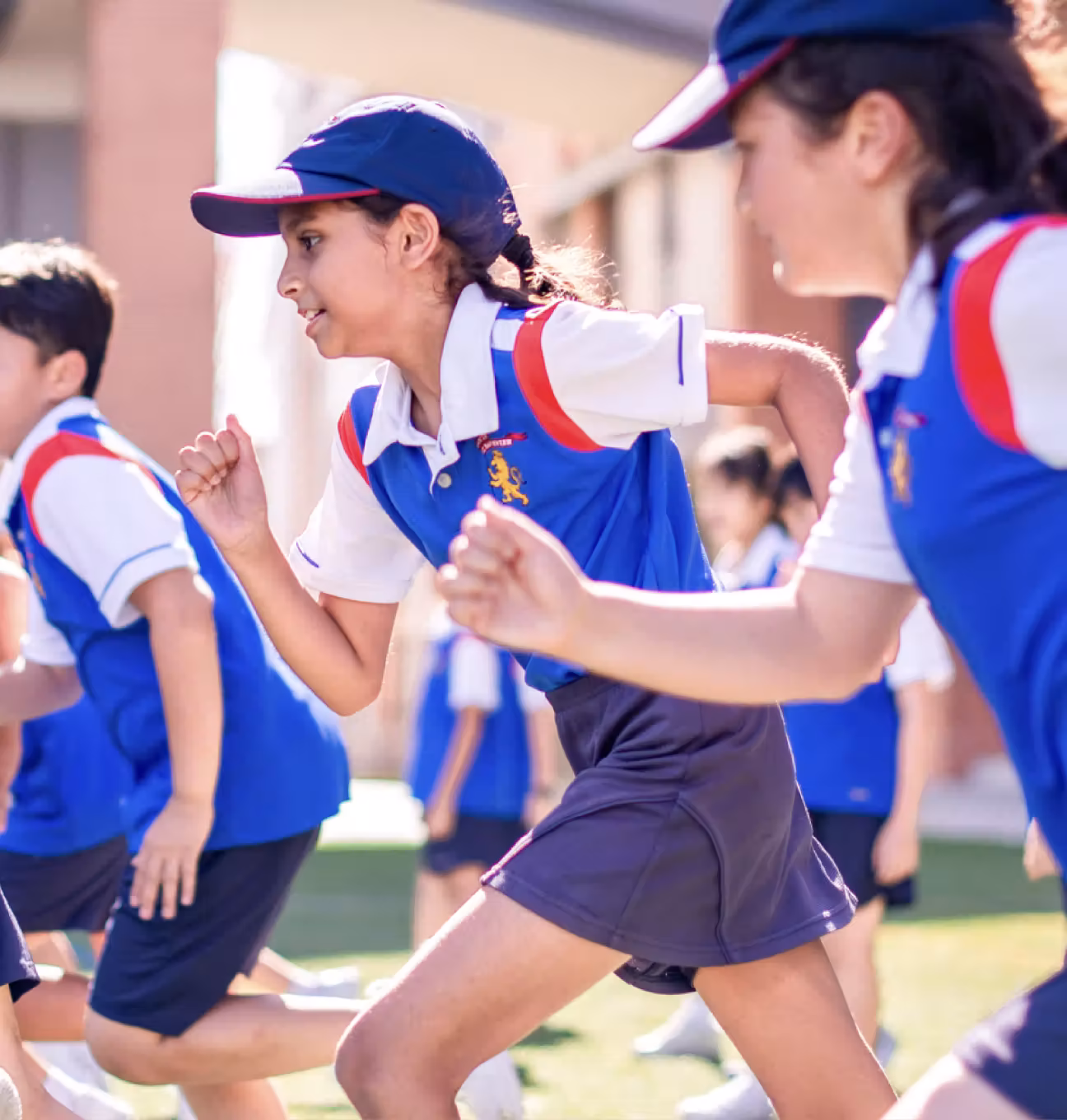 Children in blue and white sports uniforms running outdoors on grass during a game or race.