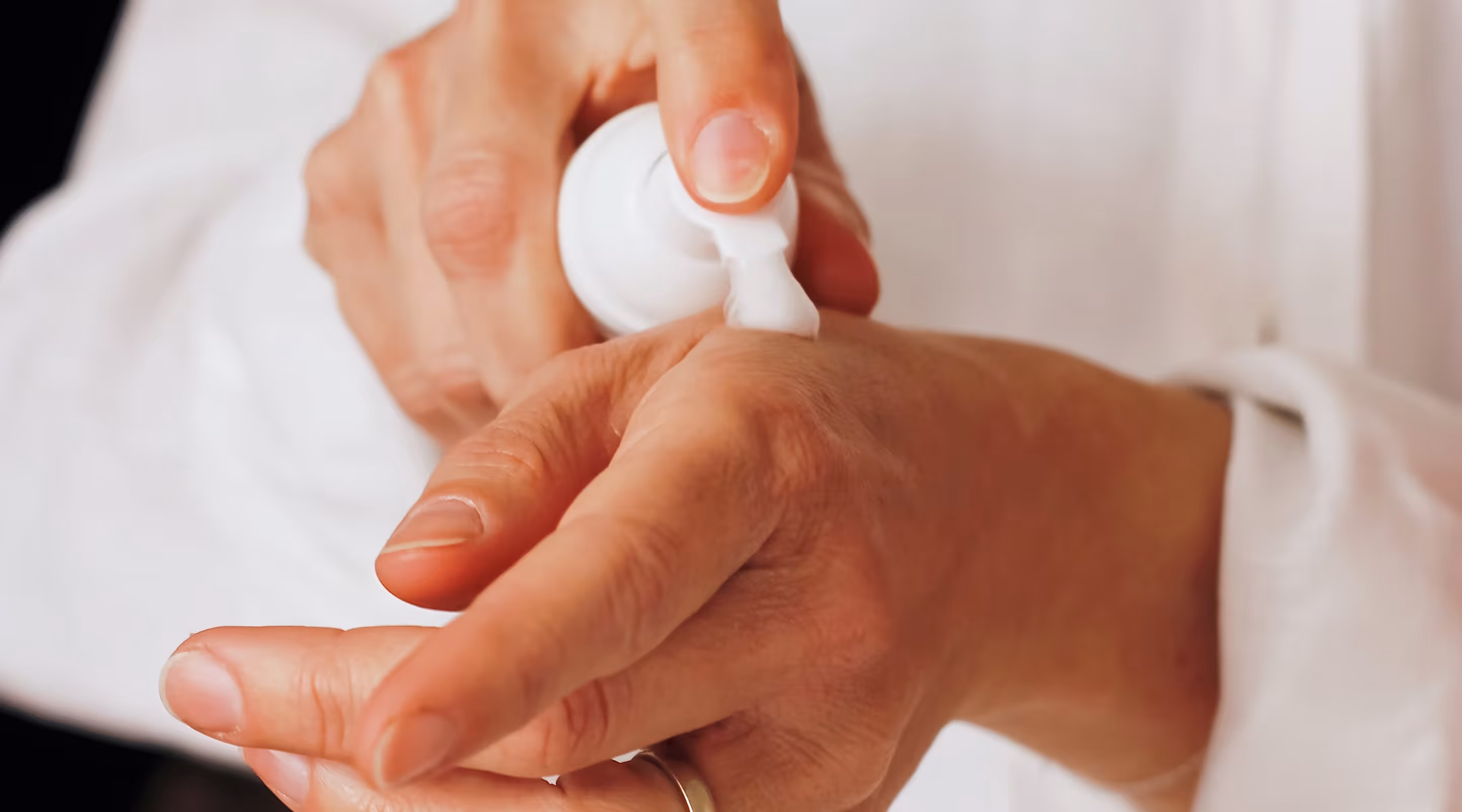 Person applying white cream or lotion on the back of their hand.