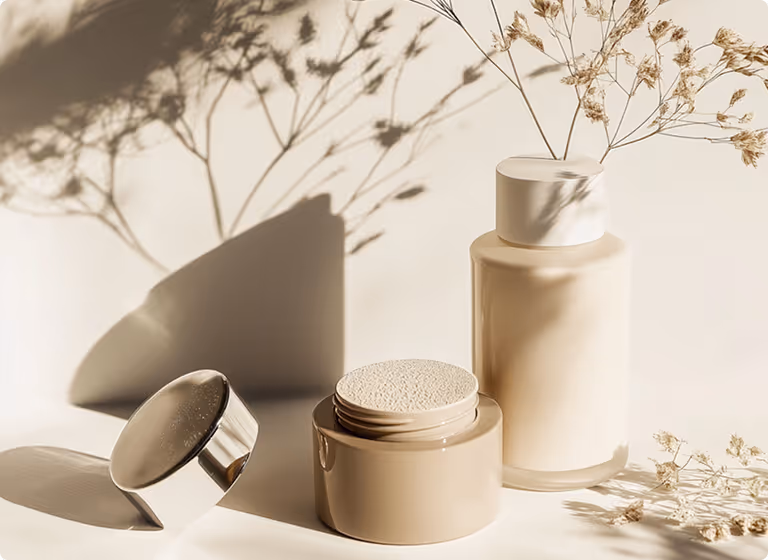 Two beige cosmetic containers with dried flowers casting shadows in soft natural light.