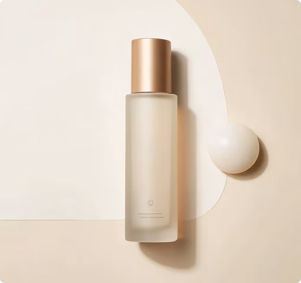 Frosted glass cosmetic bottle with a metallic gold cap on a beige and cream background with a round white object.