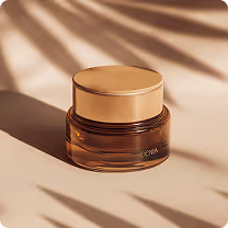 Brown and gold cosmetic jar casting shadows on a beige surface with leaf shadows in the background.