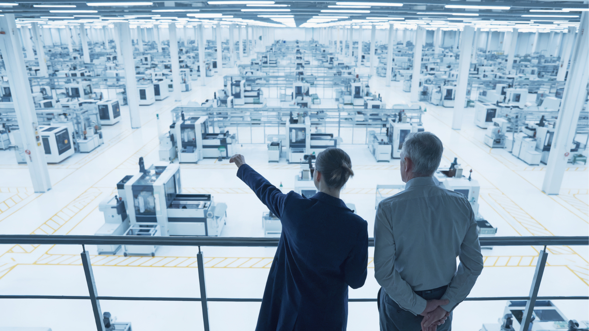 Two warehouse staff members viewing warehouse operations from an elevated vantage point, pointing out stock areas below