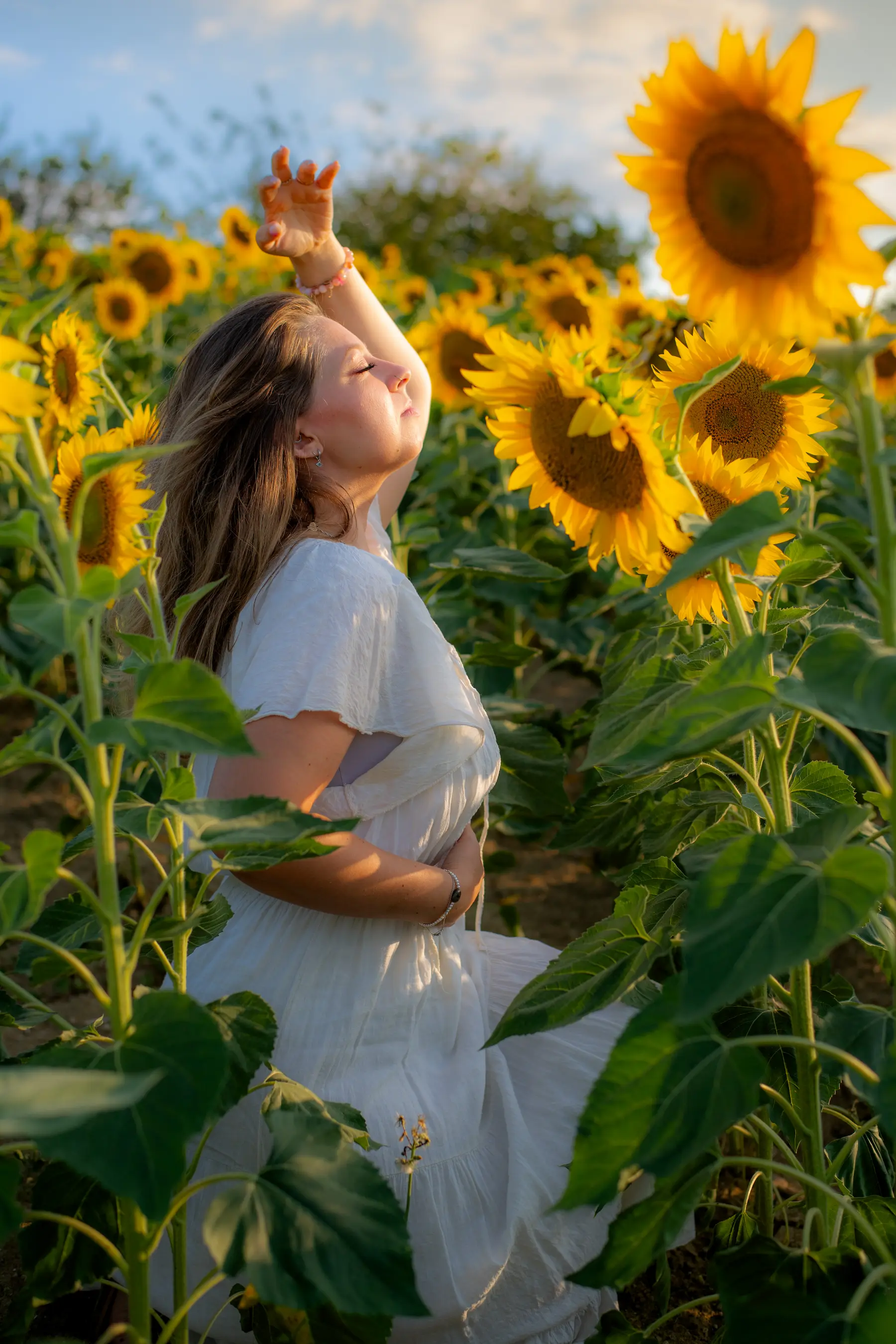 Aline Monneret debout dans un champ de tournesols, visage tourné vers la lumière, cheveux au vent.