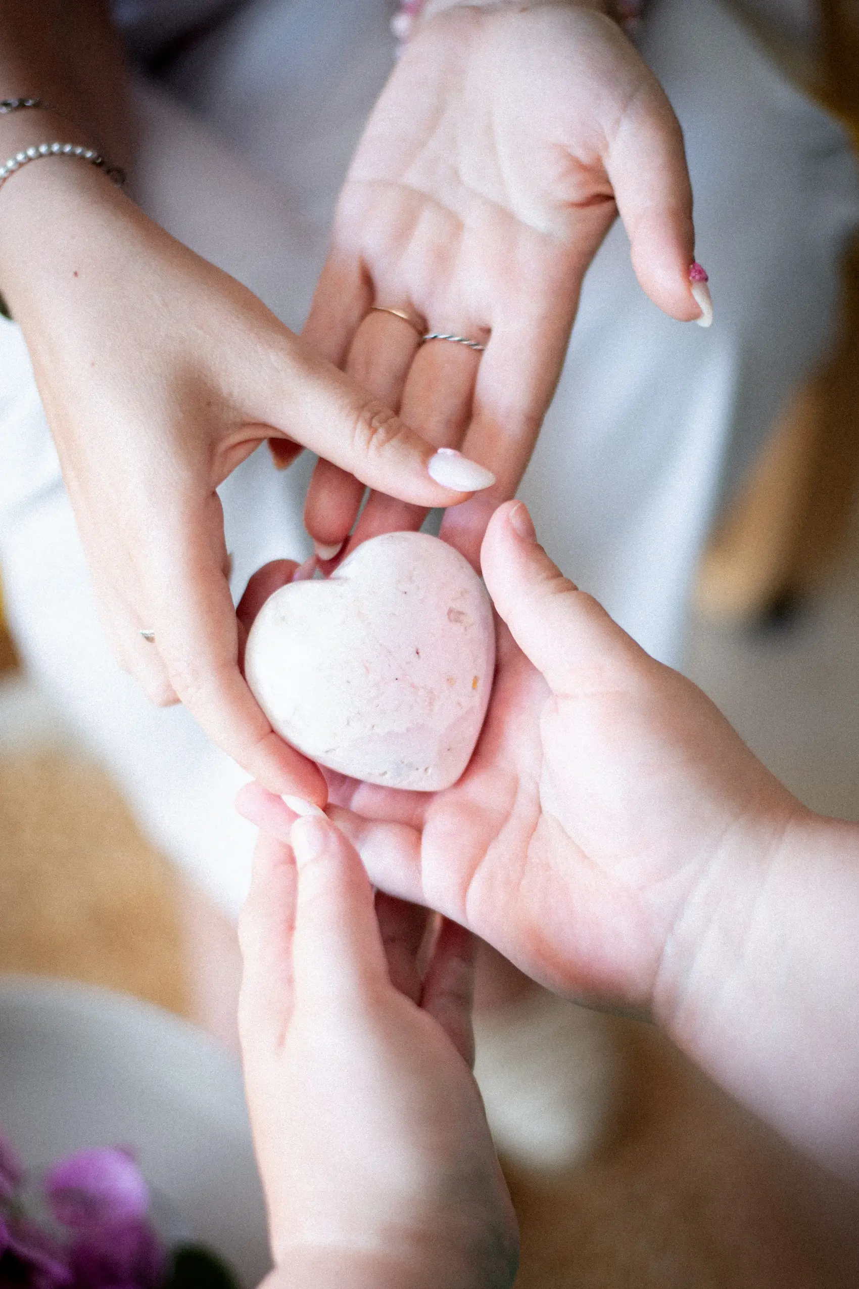 Deux mains formant un cœur autour d’une pierre rose, symbole de douceur et de soin.