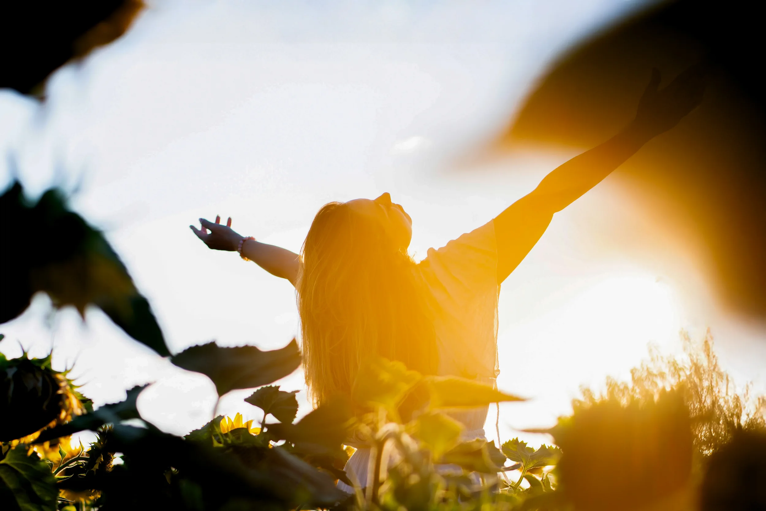 Aline Monneret, psychopraticienne, bras ouverts dans un champ de tournesols — symbole d’apaisement.