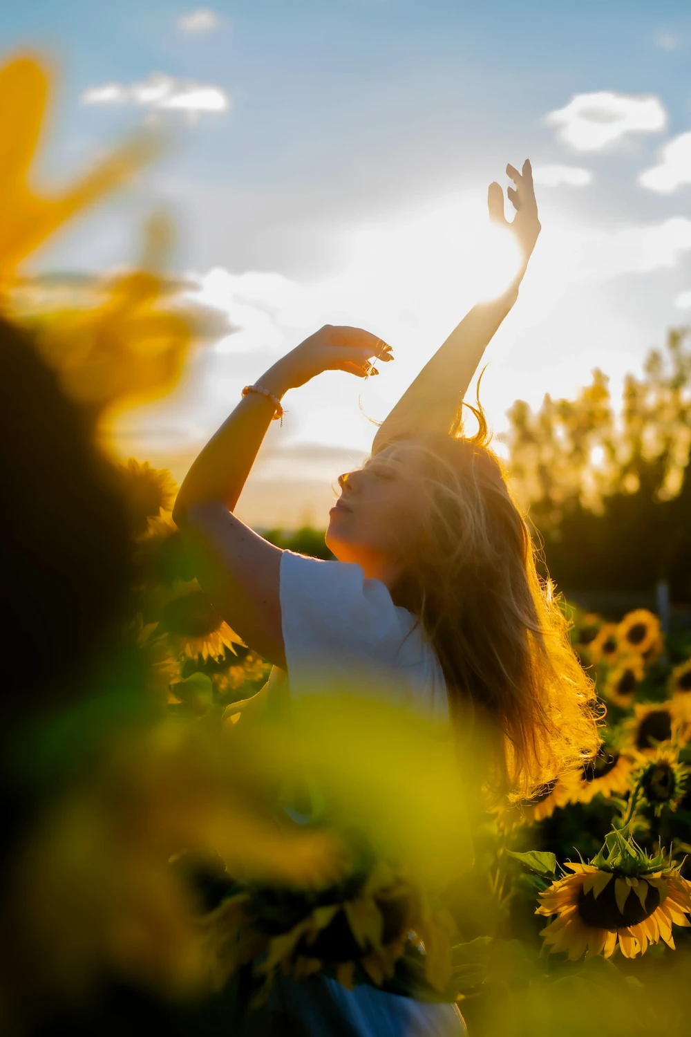 Aline Monneret, psychopraticienne — image d’apaisement et de reconnexion : femme les bras levés parmi les tournesols.