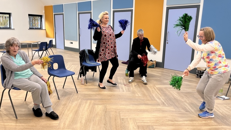 People dancing in a circle using pom-poms at dementia dance class