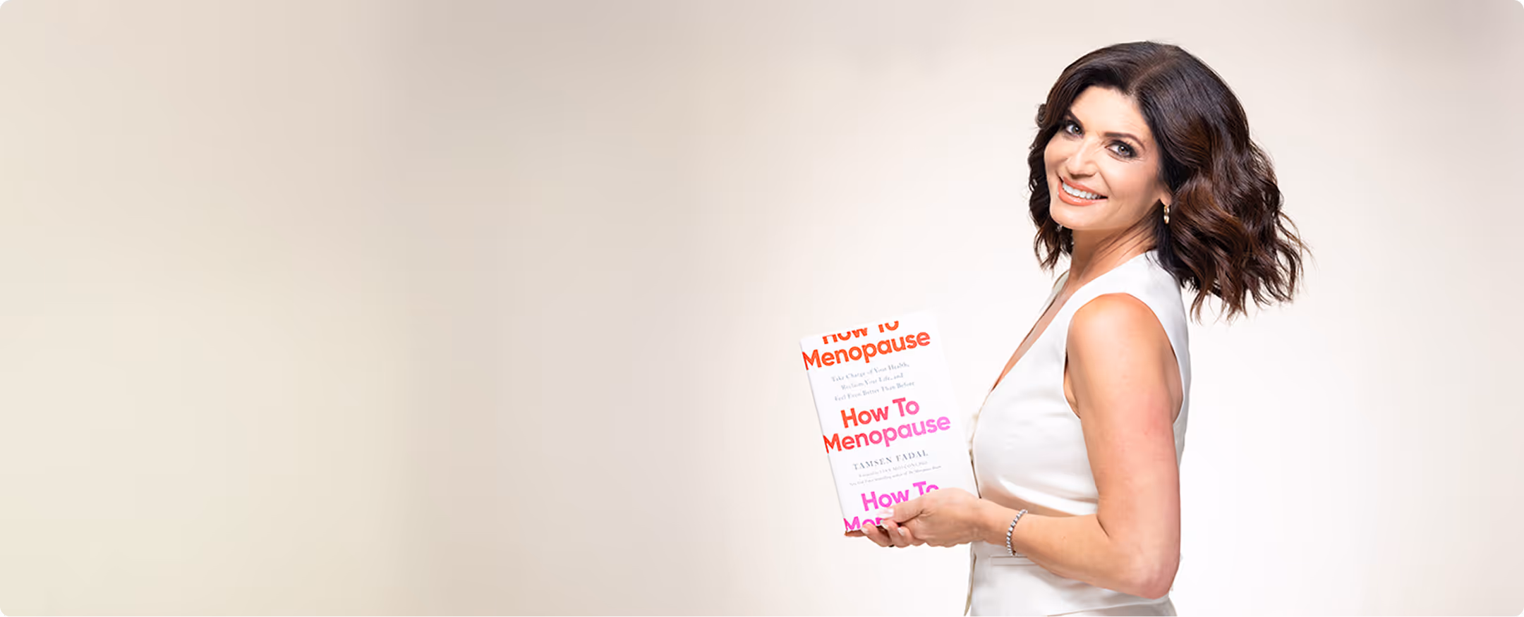 Smiling woman in white sleeveless dress holding a book titled 'How To Menopause' against a light beige background.