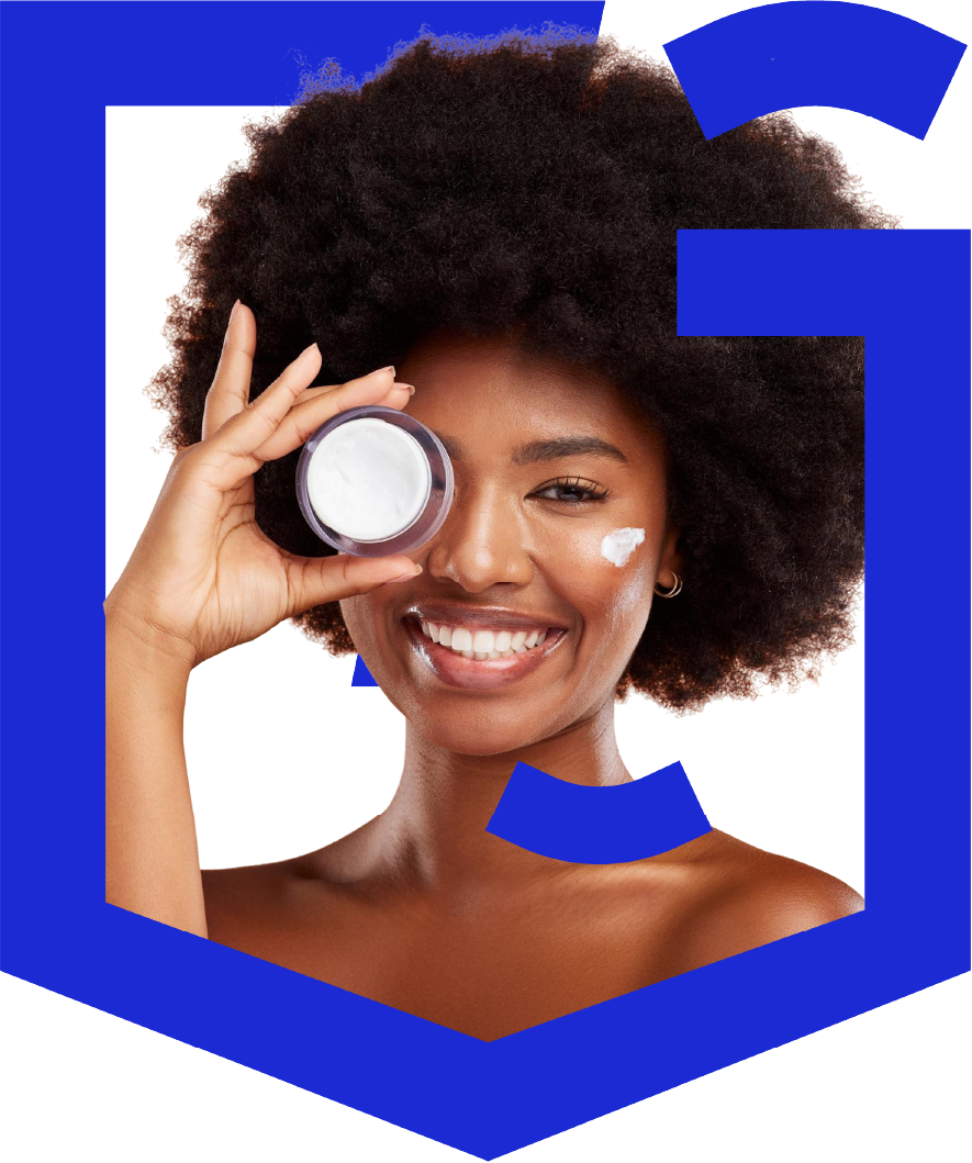 A woman with a white face and black hair is smiling and holding a jar of lotion.