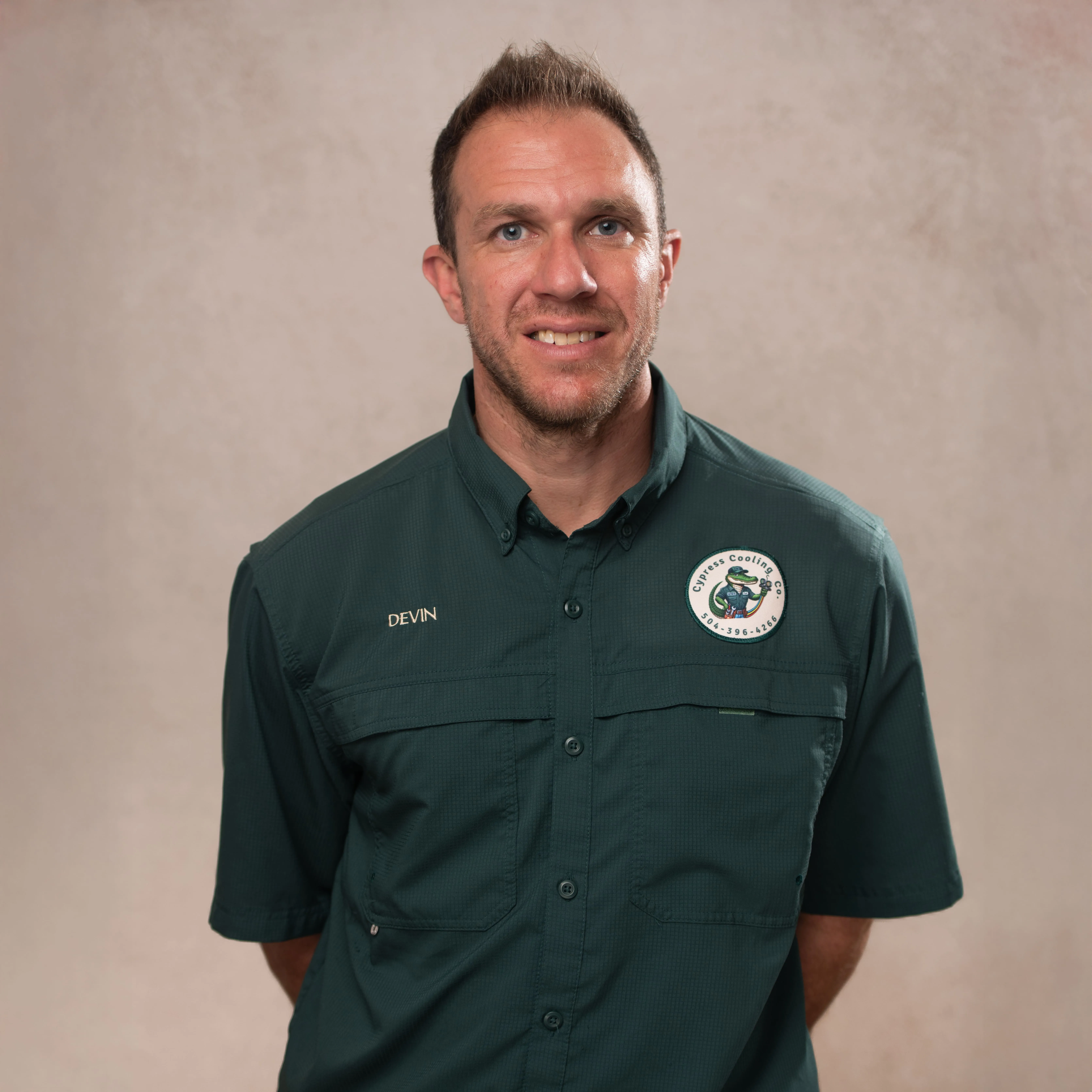 Man wearing a dark green Cypress Cooling Co. shirt with the name Devin embroidered on it, standing against a plain background.