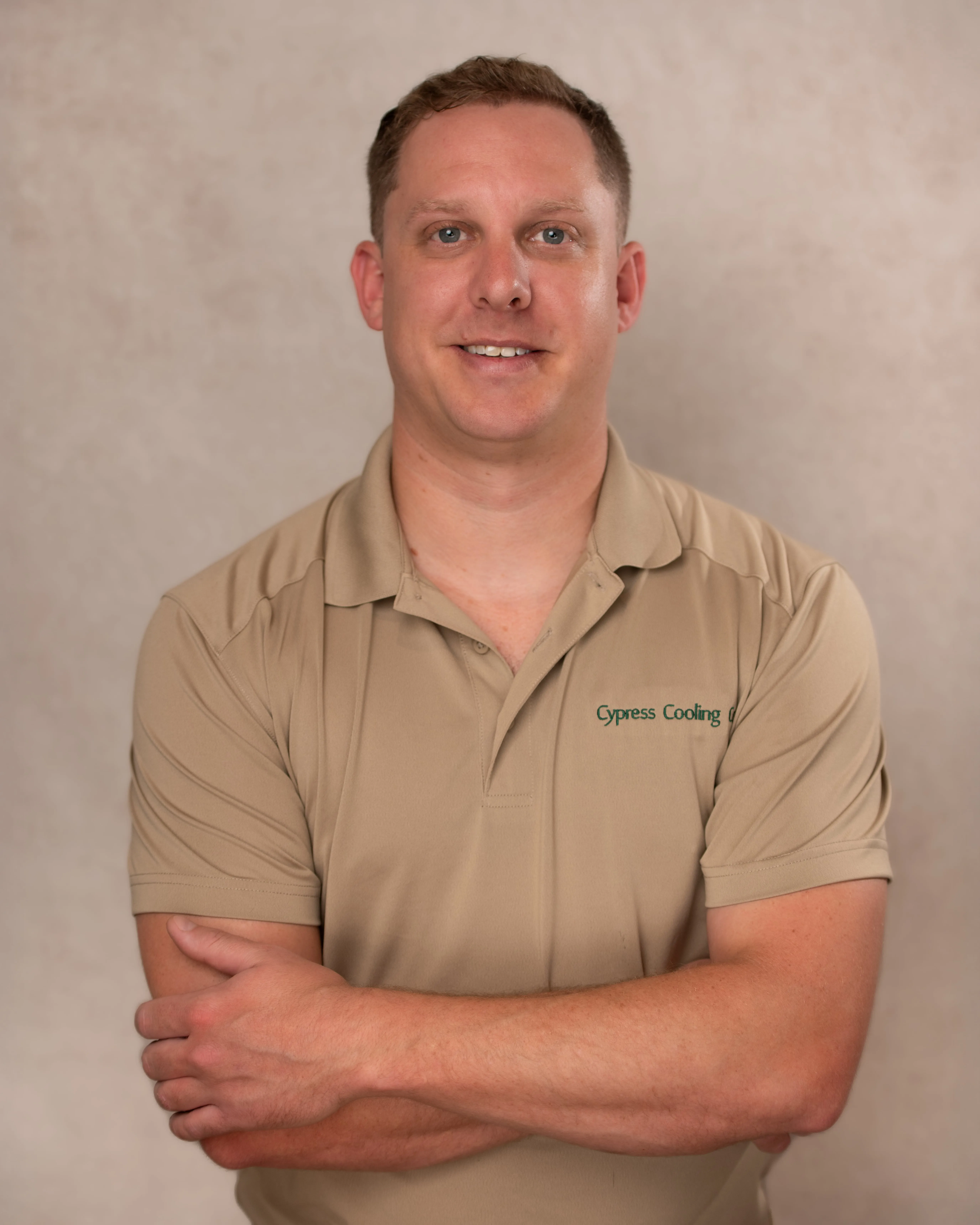 Man with short blonde hair wearing a tan polo shirt with 'Cypress Cooling' logo, smiling with arms crossed.