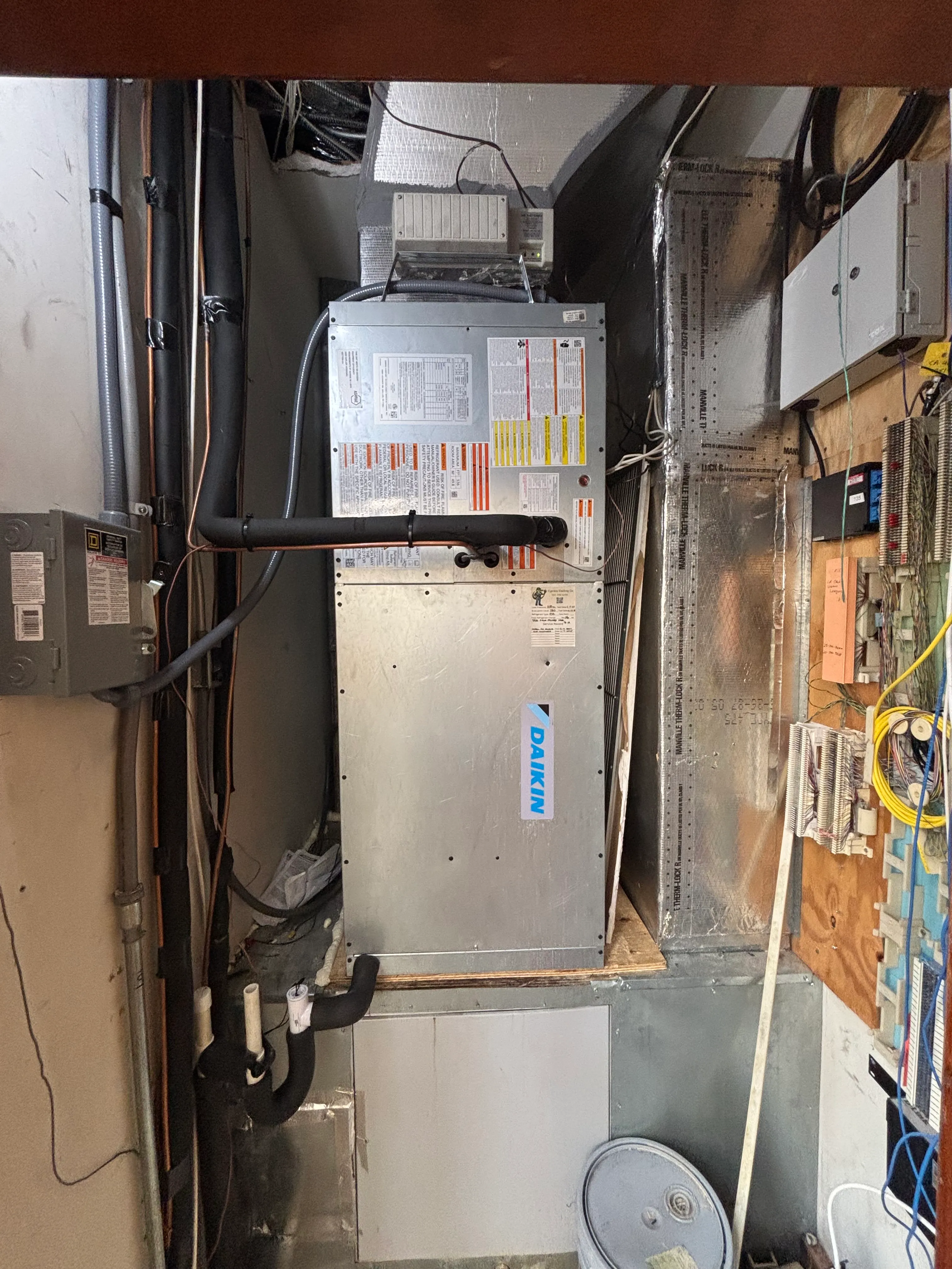 Daikin air conditioning unit installed in a utility room with pipes, electrical wiring, and metal ductwork.