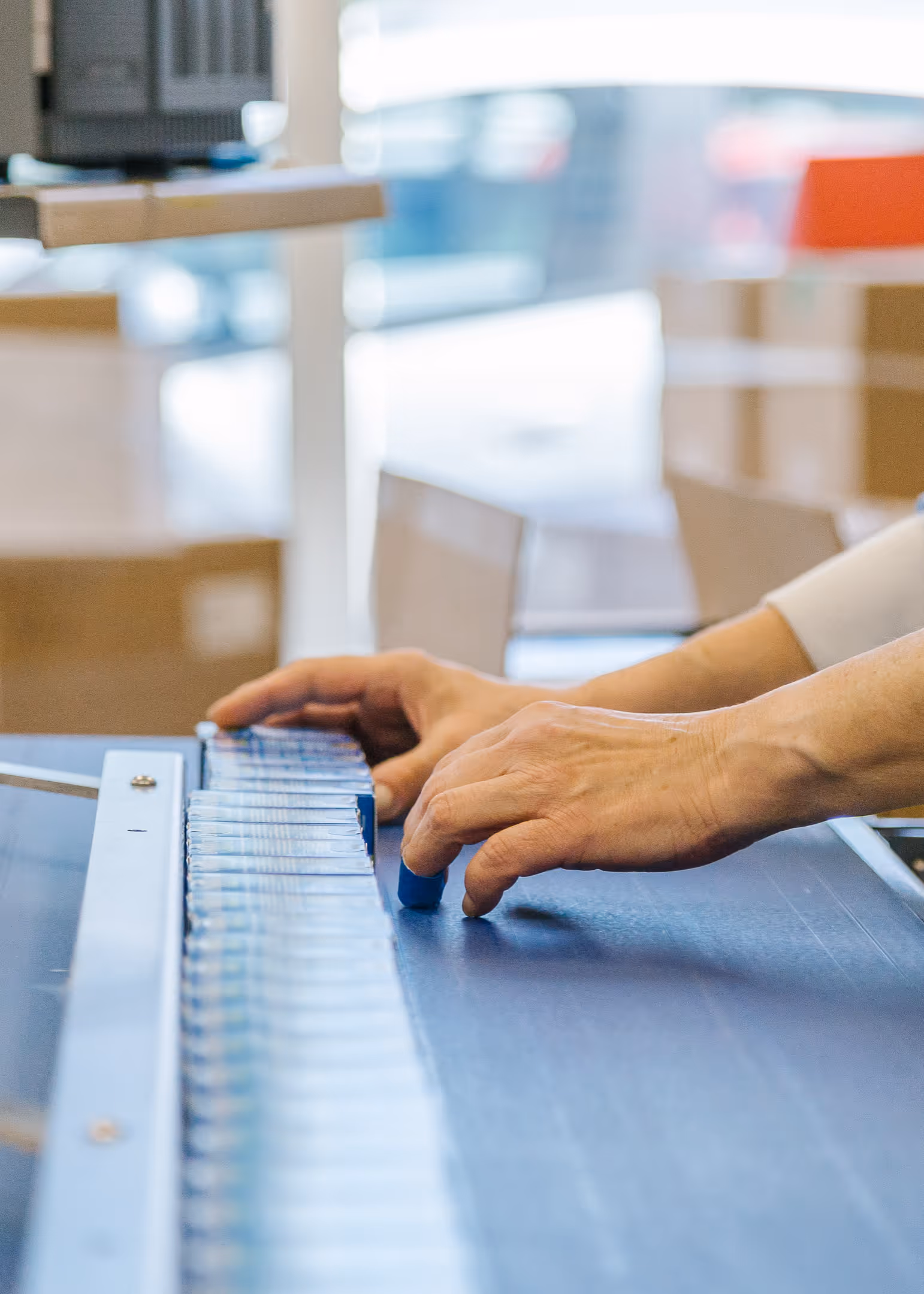 Hands arranging blue files in a row on a conveyor belt in an office environment. The background is softly blurred, creating a focused and orderly atmosphere.