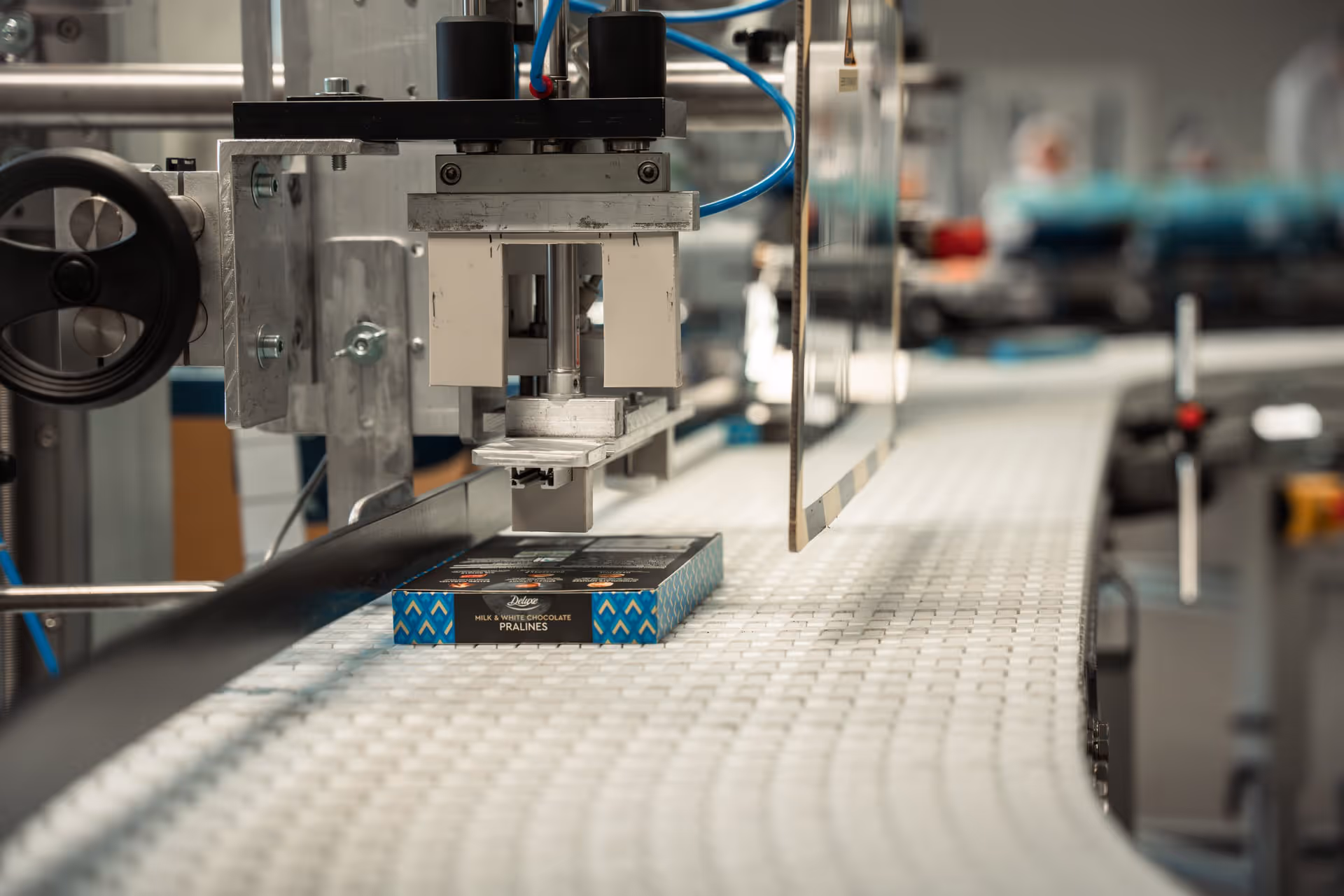 A robotic arm on an assembly line carefully handles a box of chocolates, reflecting a modern, efficient, and precise industrial packaging process.