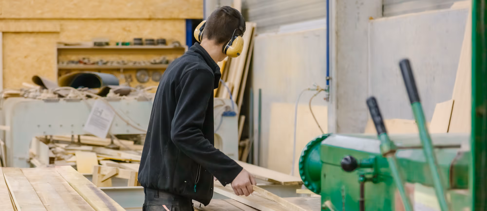 Man wearing ear protection working on wooden planks in a carpentry workshop.