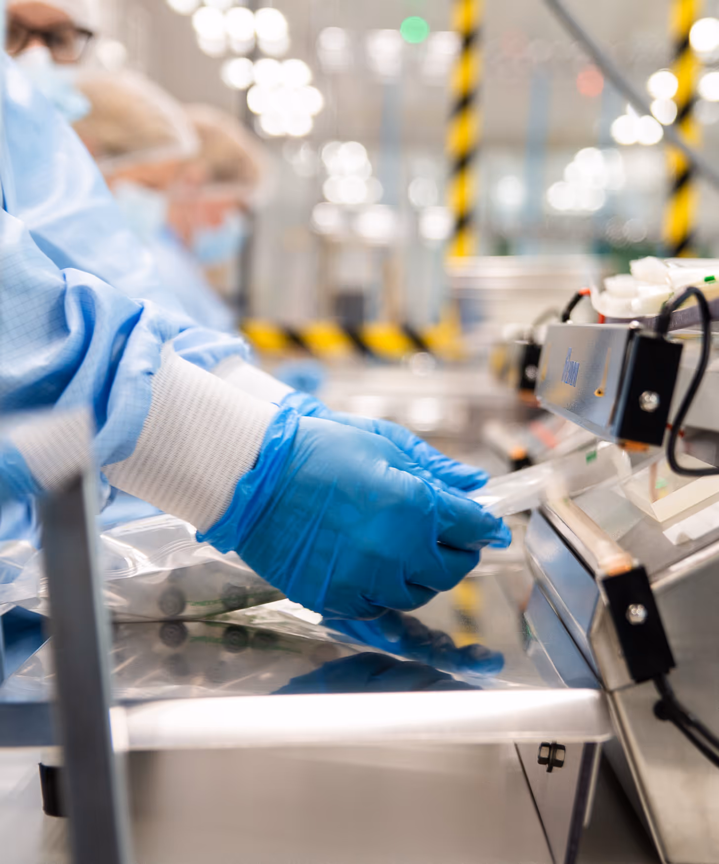 A laboratory assistant wearing protective clothing operates machines that seal items in sterilization bags. The environment is clean and focused, conveying a sense of precision.